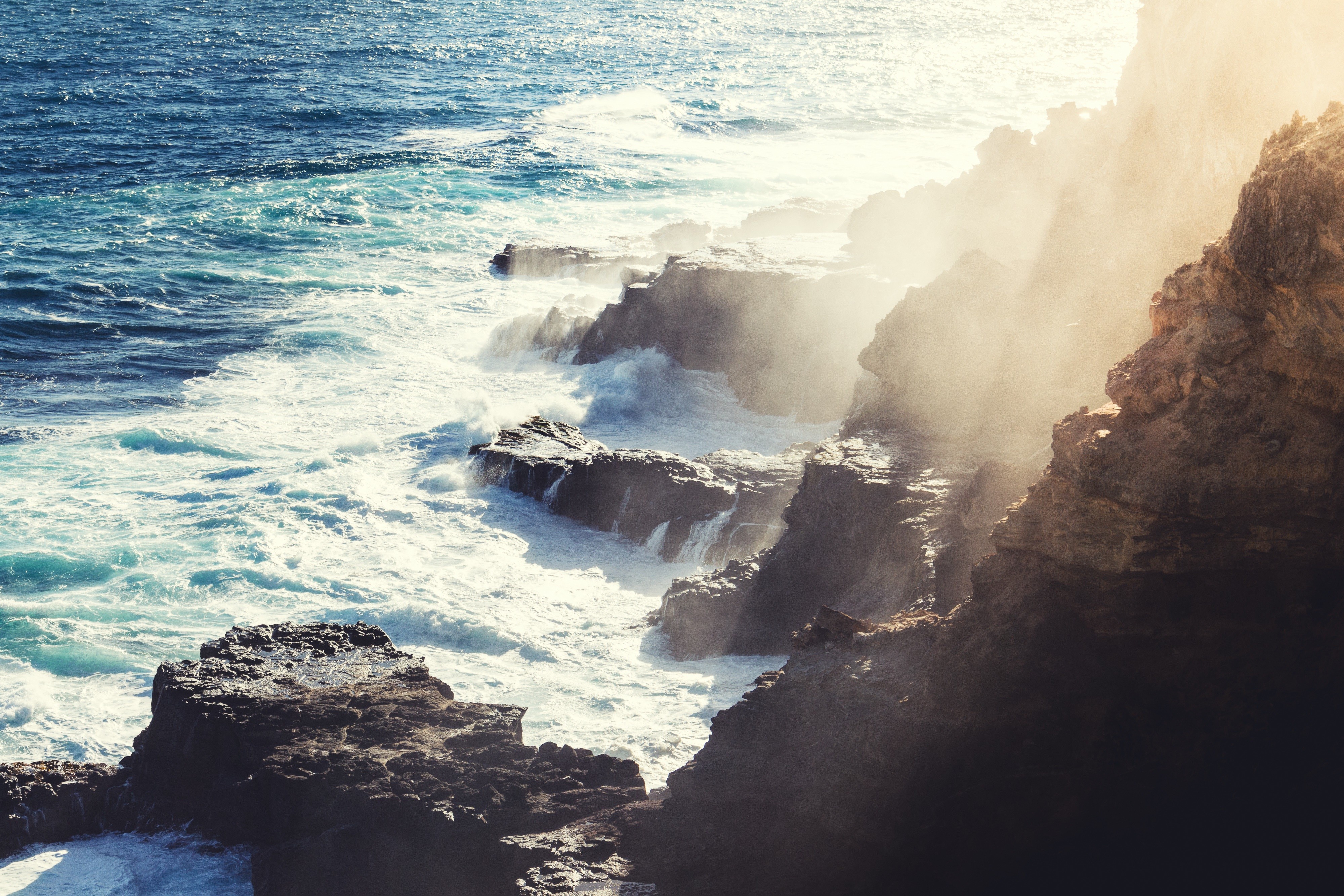Waves crashing on rocky cliffs with sunlight HD Wallpaper