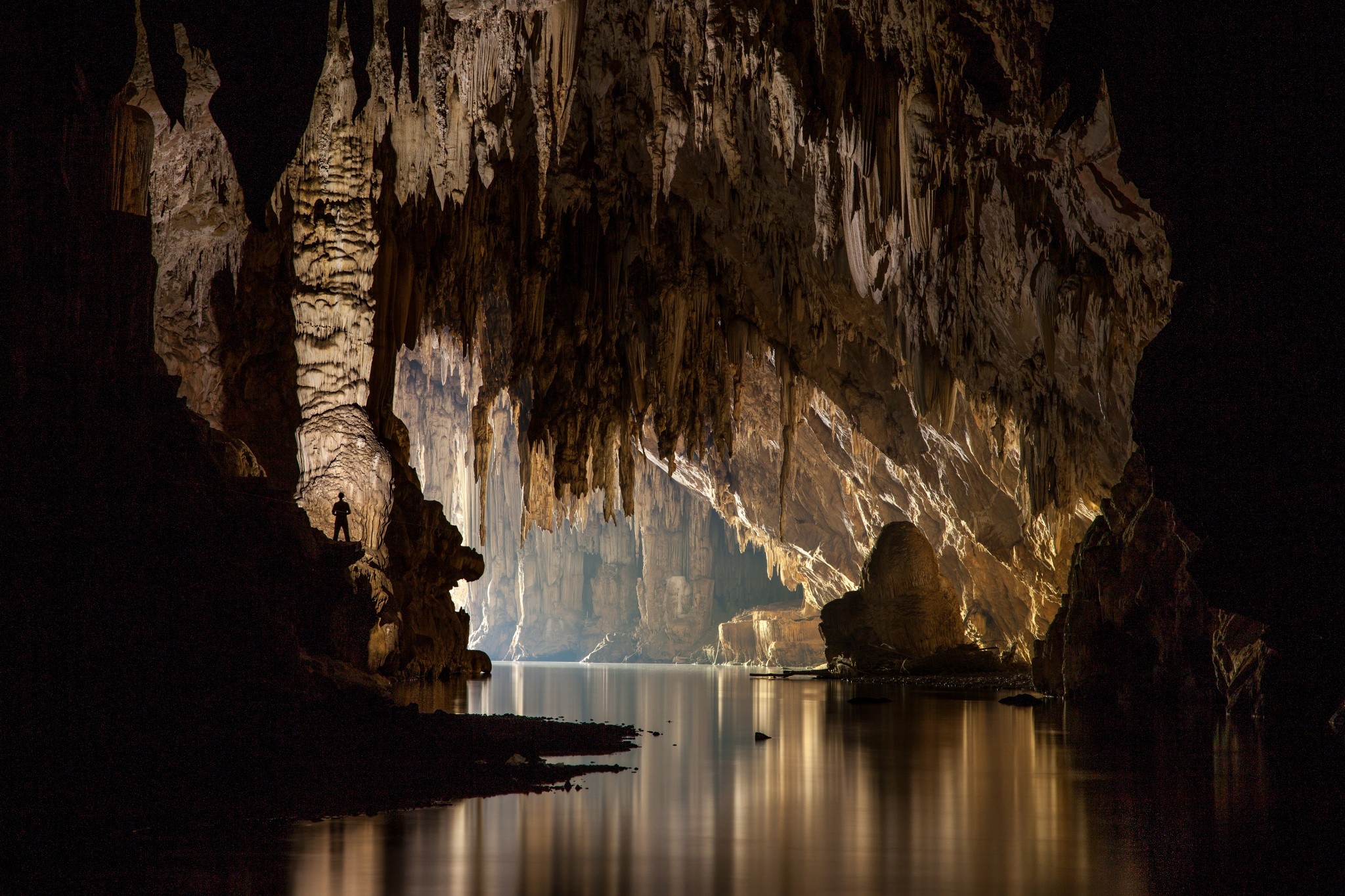Man standing in a vast cave with a body of water HD Wallpaper