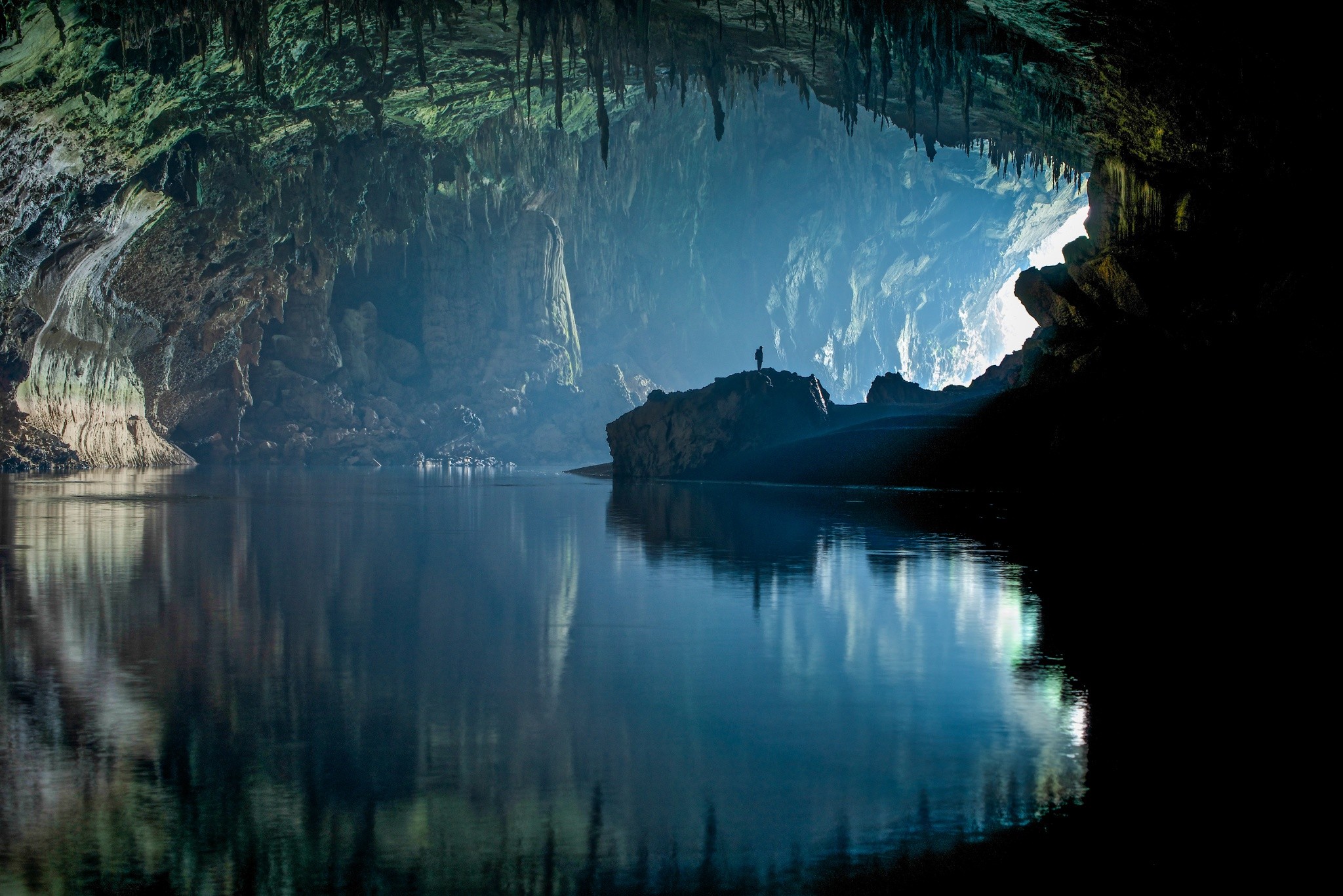 Man standing on rock in a vast cave with water HD Wallpaper