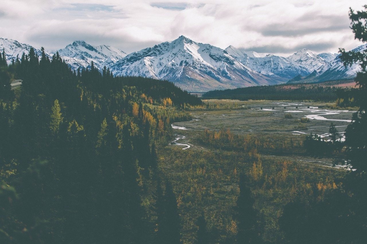 Snow-capped mountains and a winding river in a forest valley HD Wallpaper