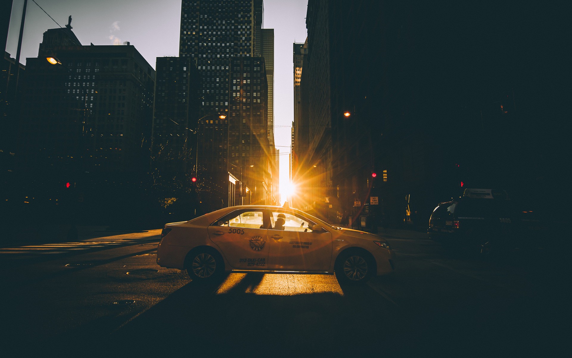 Yellow taxi driving down a city street at sunset HD Wallpaper