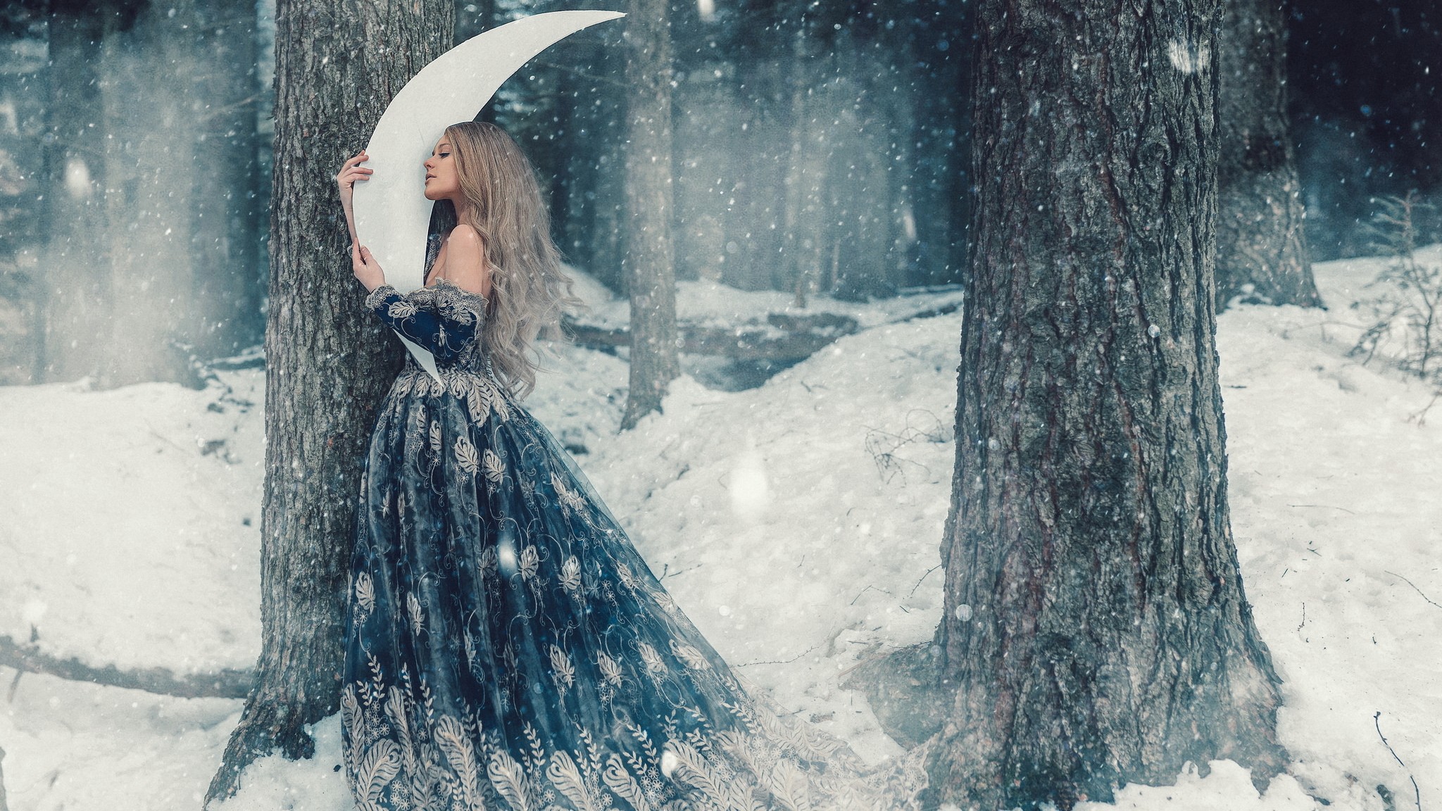 Woman in a blue dress holding a crescent moon in a snowy forest HD Wallpaper