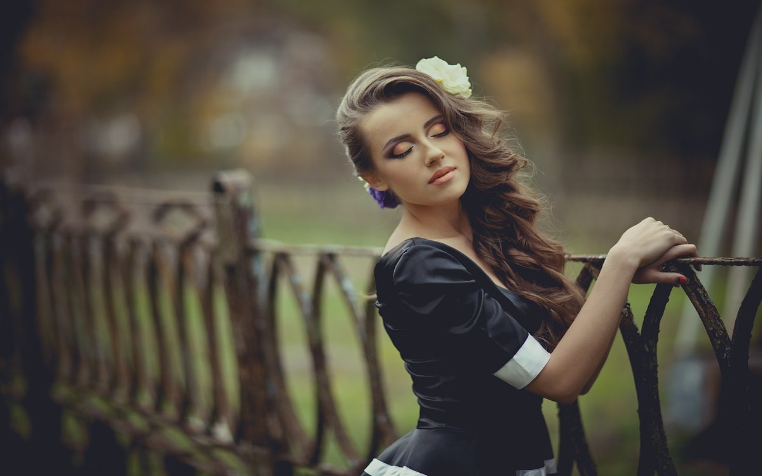 Woman with flower in hair by a fence HD Wallpaper