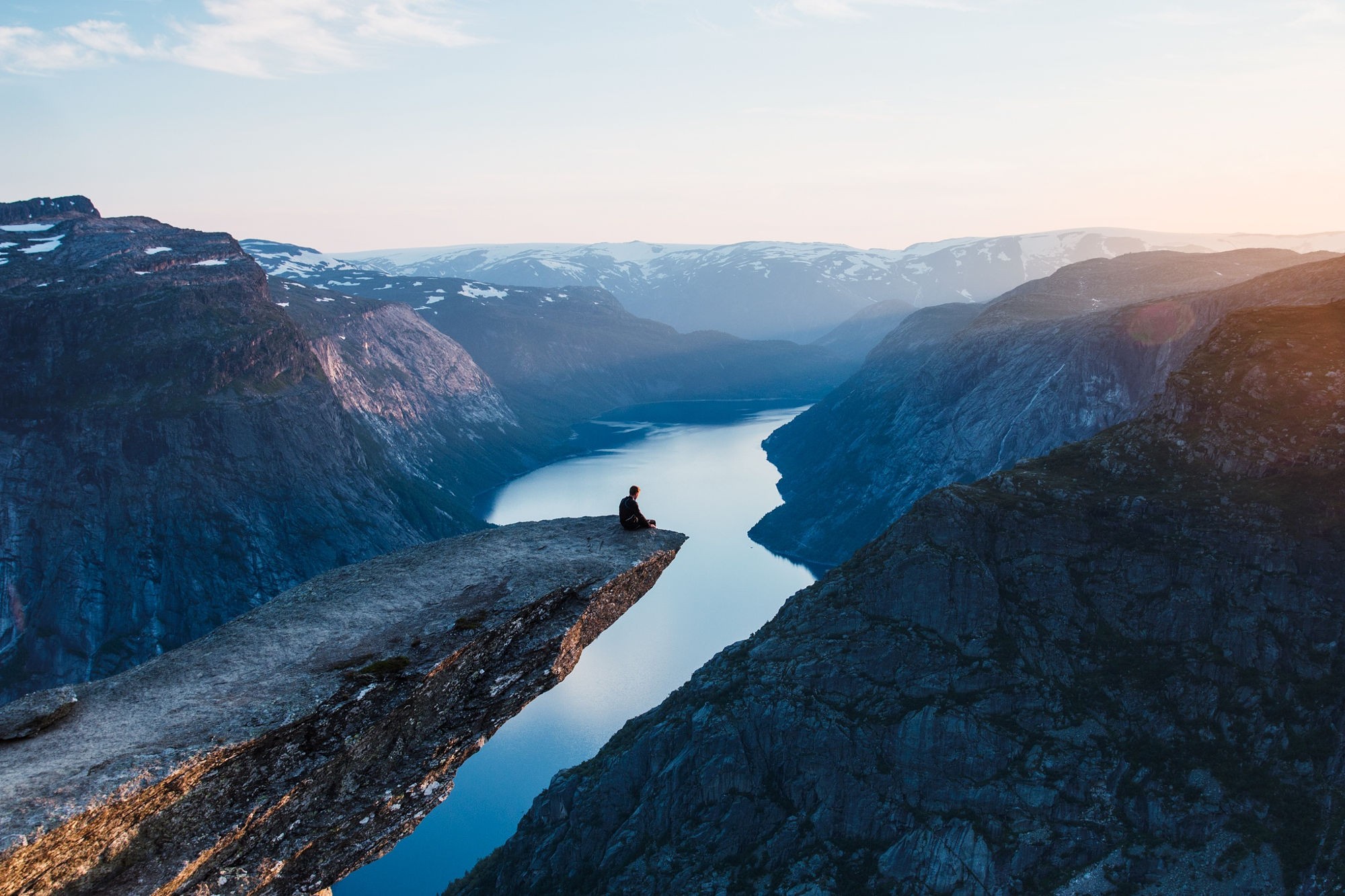 Person sitting on Trolltunga cliff overlooking a fjord in Norway HD Wallpaper