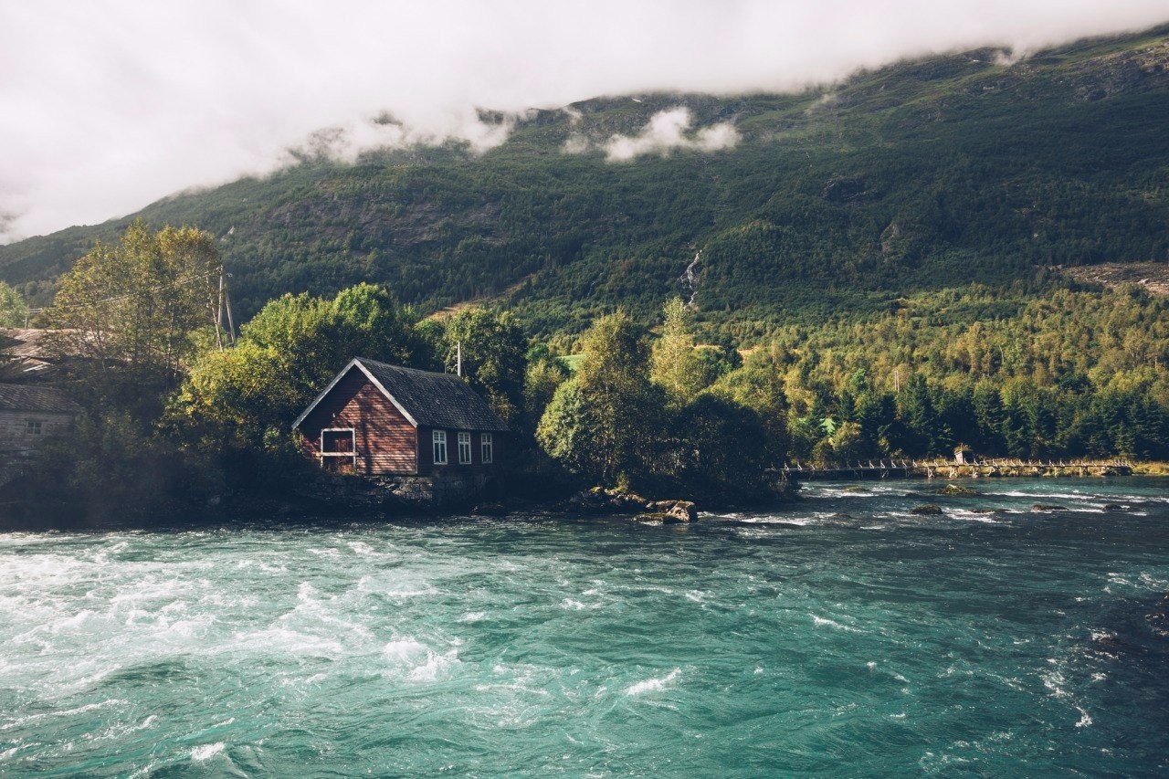 Wooden house by a river in a mountainous forest HD Wallpaper