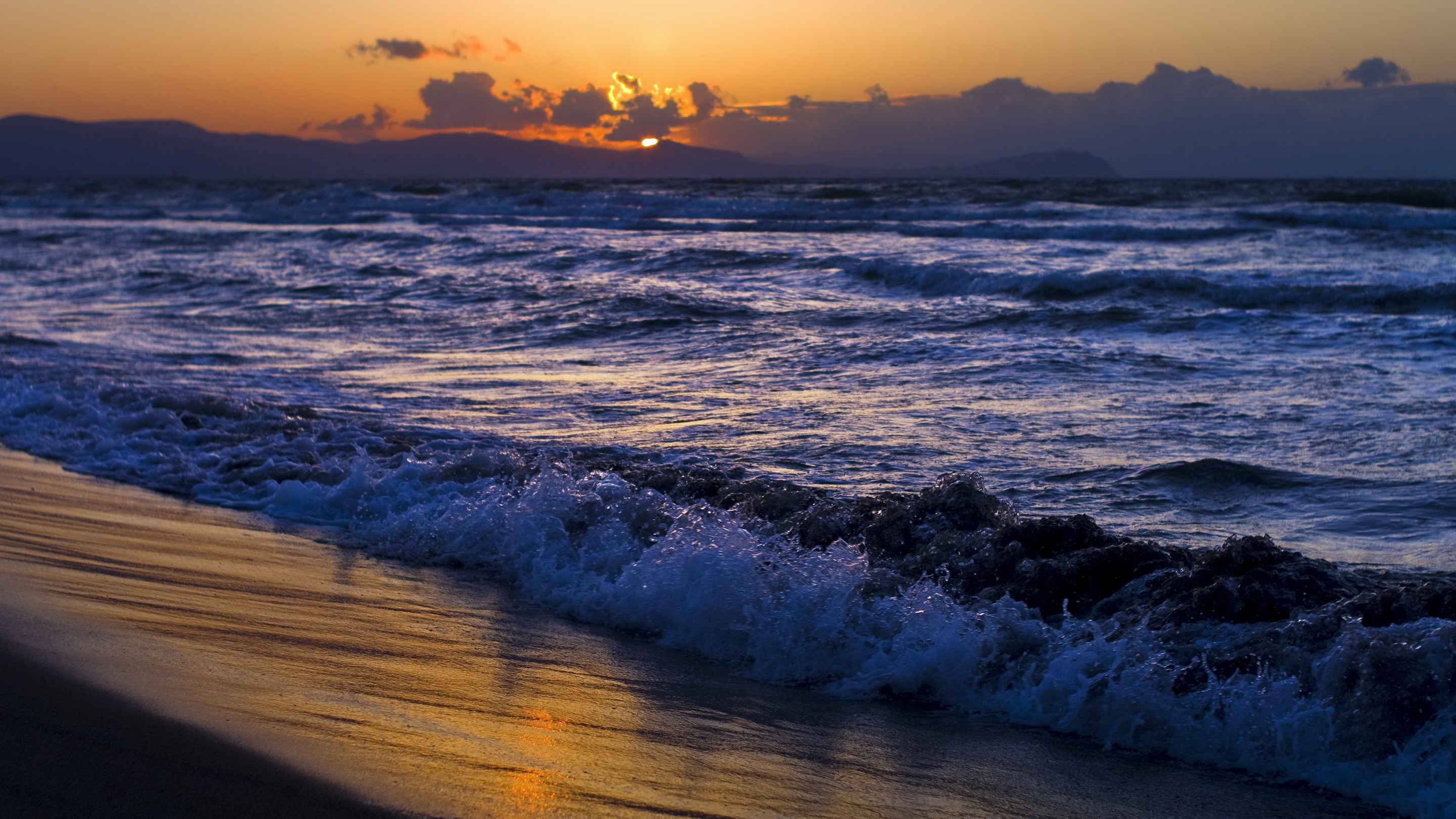 Sunset over the ocean with waves crashing on the beach HD Wallpaper