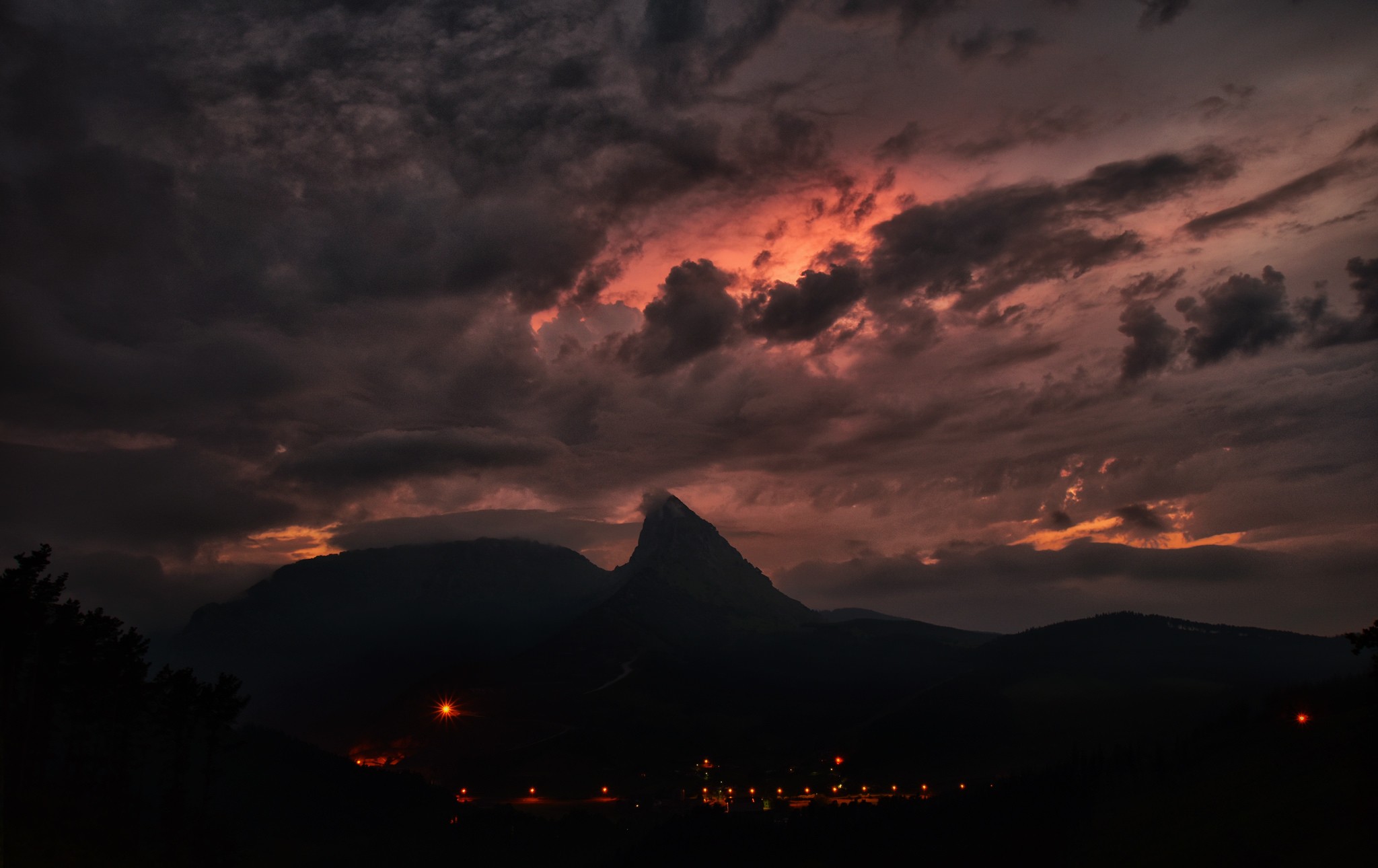 Dark clouds over mountains at night with village lights HD Wallpaper