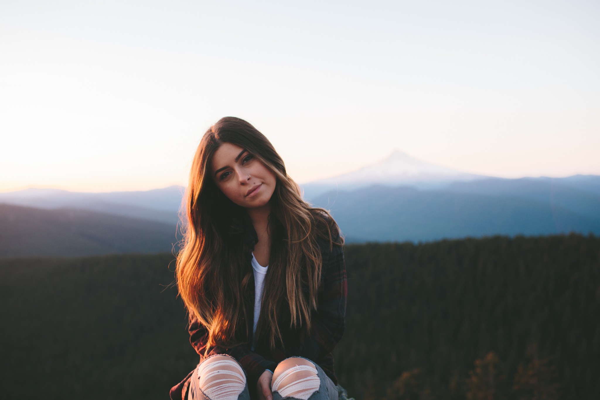 Woman with long hair sitting outdoors with mountains in background HD Wallpaper