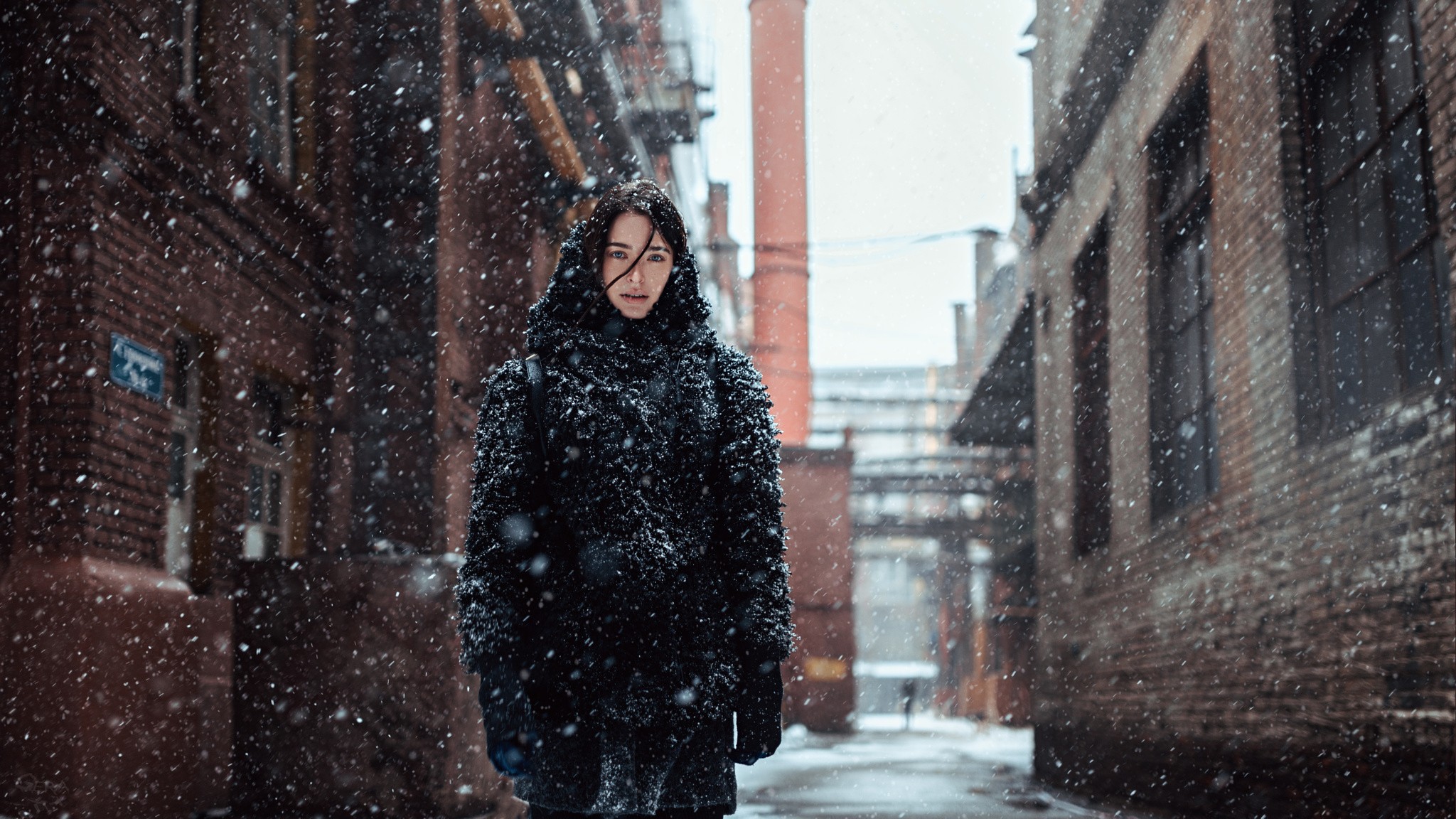 Woman in a black coat in a snowy urban alley HD Wallpaper