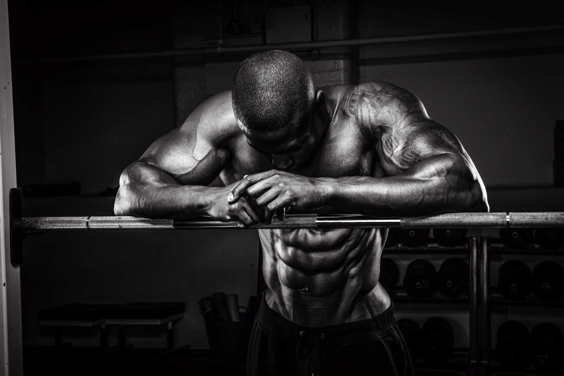 Black and white photo of a muscular man resting on a barbell HD Wallpaper