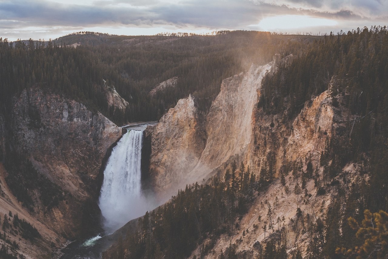 Waterfall cascading into a canyon with pine forest HD Wallpaper