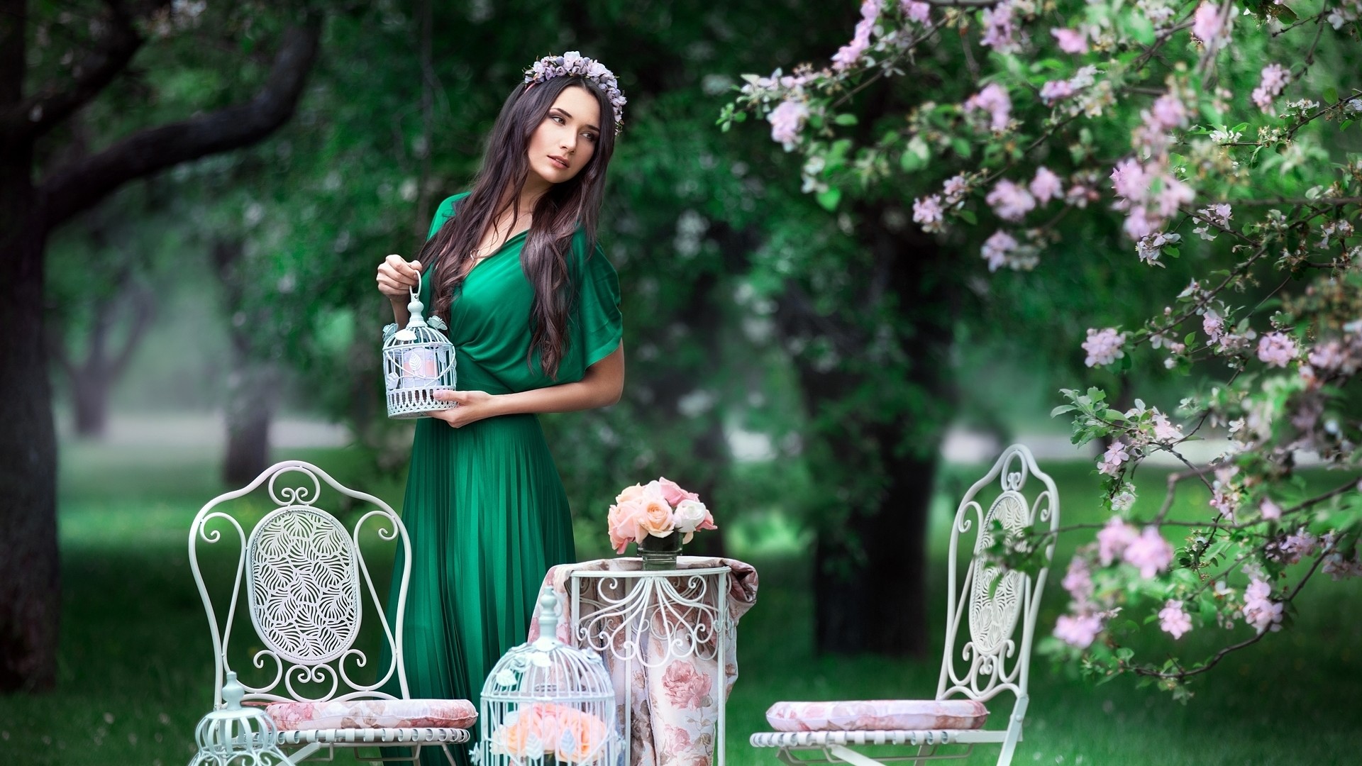 Woman in green dress holding a birdcage in a park HD Wallpaper