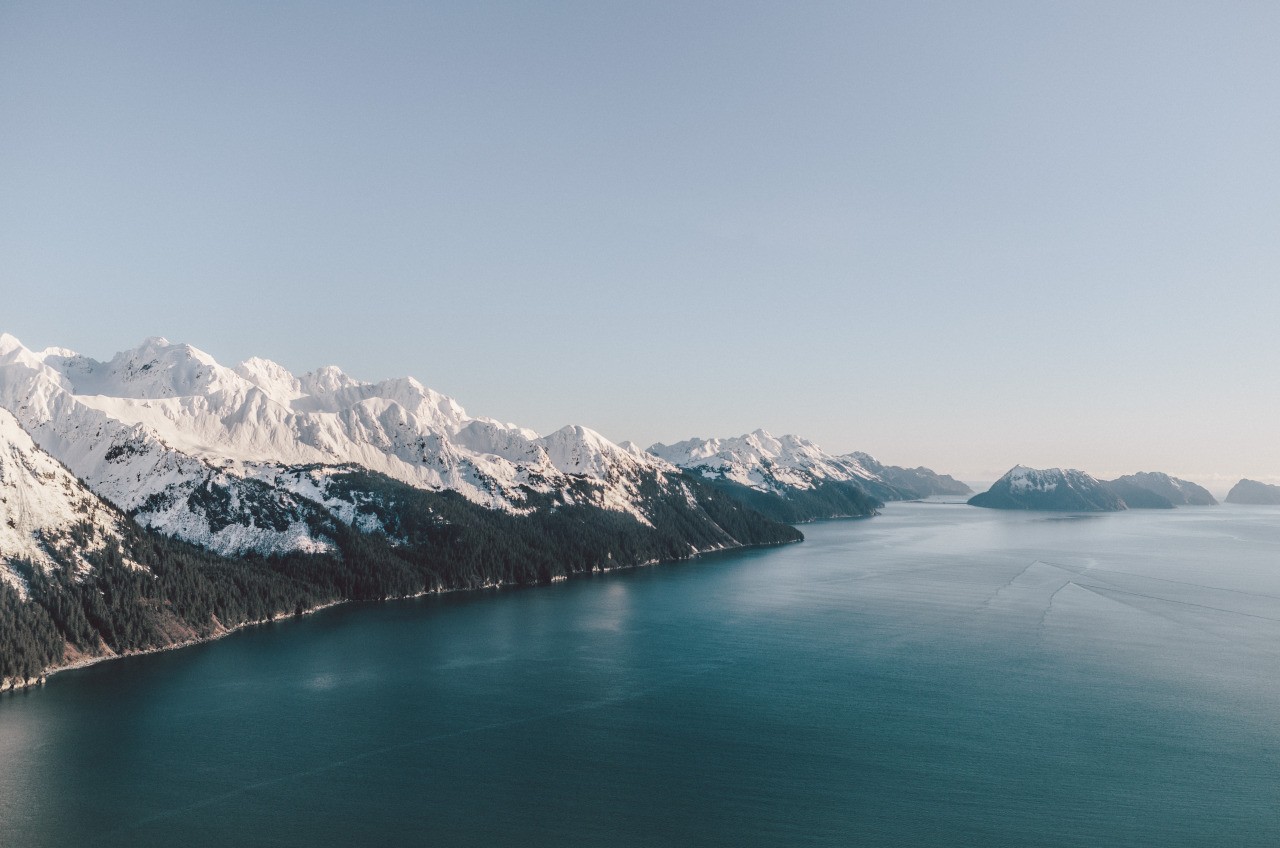 Snow-capped mountains meet a vast blue ocean HD Wallpaper