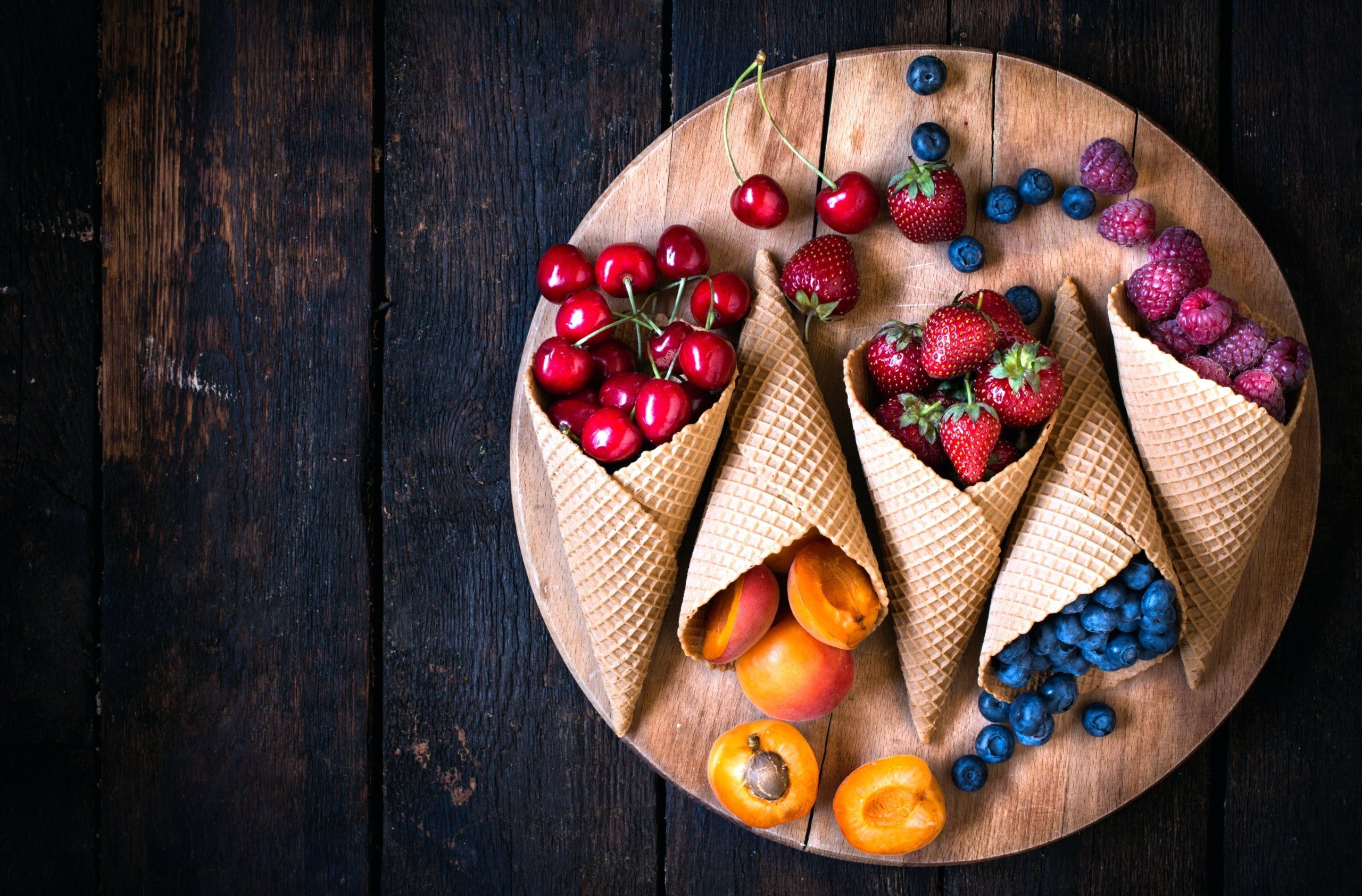 Waffle cones filled with fresh berries and apricots on a wooden board HD Wallpaper