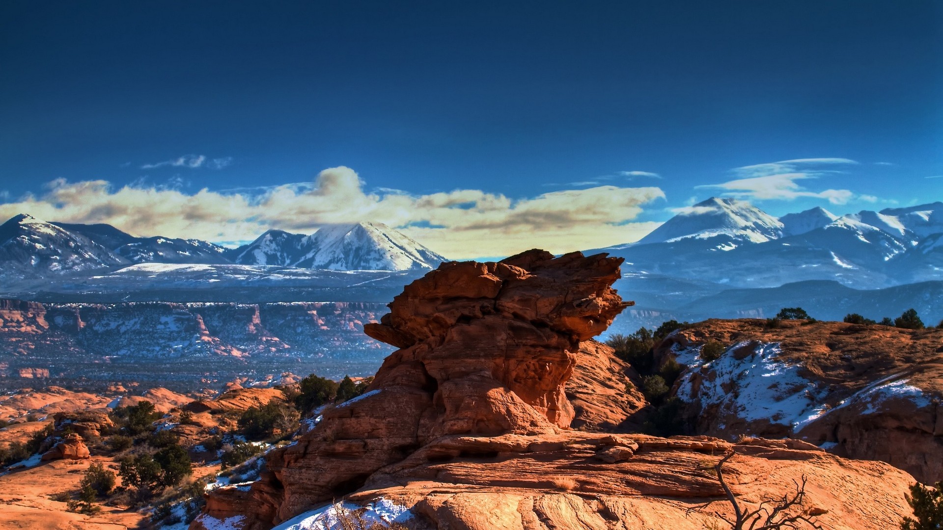 Snowy mountain peaks behind a rocky desert landscape HD Wallpaper