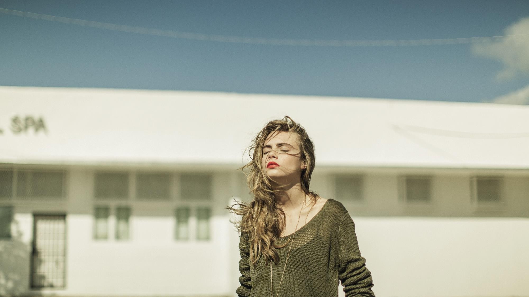 Cara Delevingne with eyes closed in front of a building HD Wallpaper