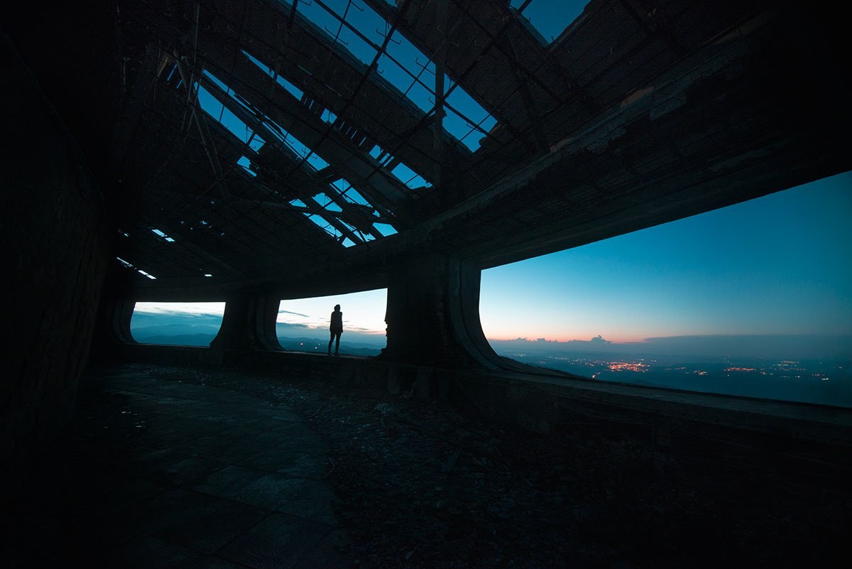 Silhouette of a person in a ruined building overlooking a city at dusk HD Wallpaper