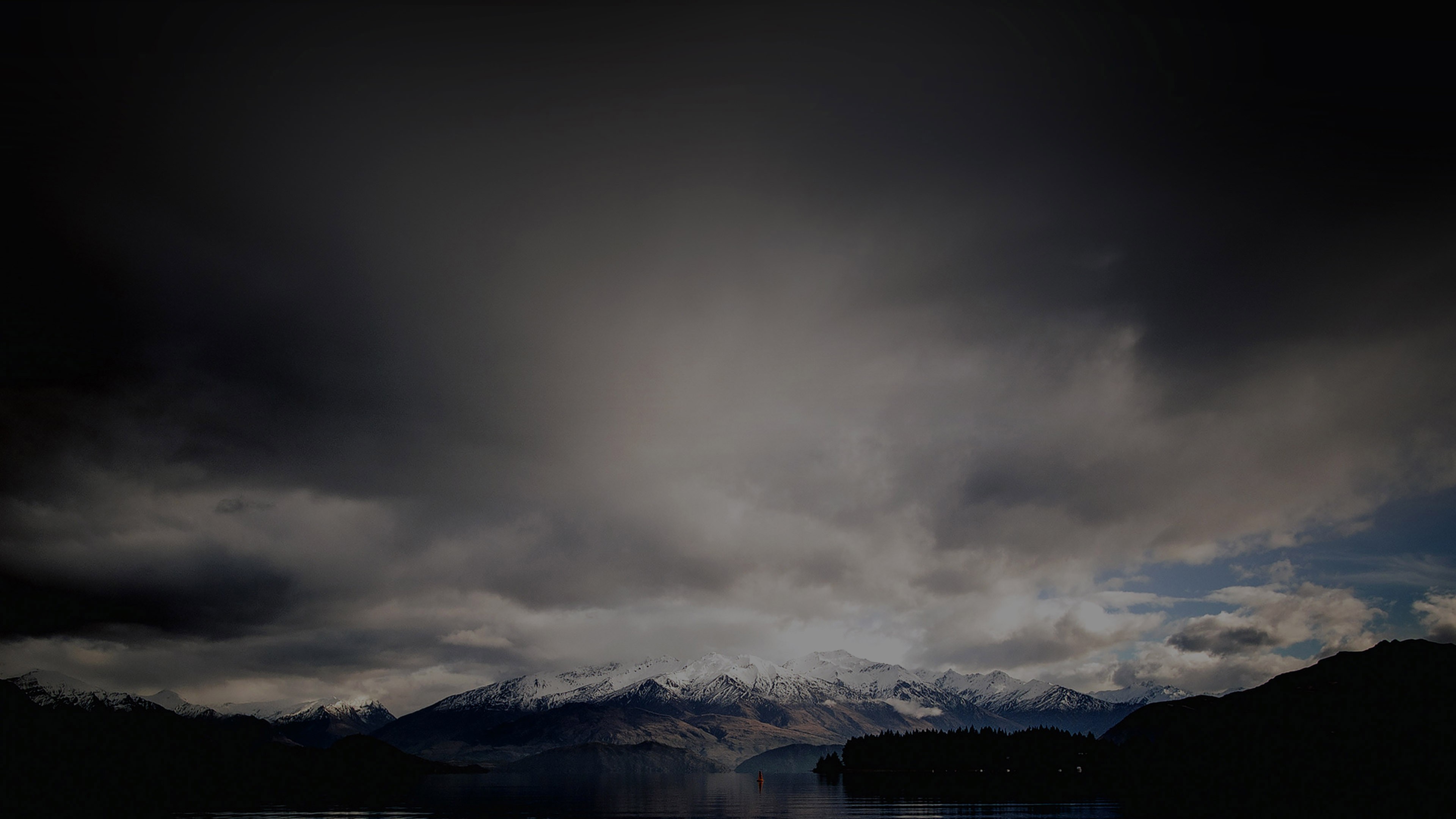 Snow-capped mountains over a dark lake under stormy clouds HD Wallpaper