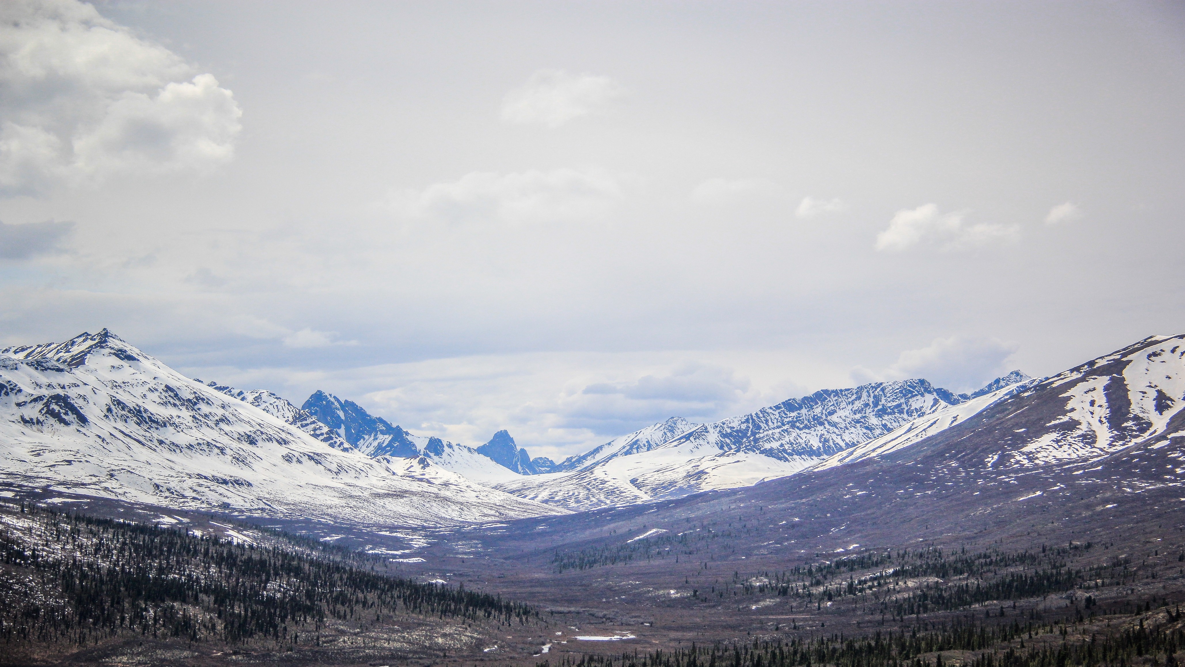 Snow-capped mountains under a cloudy sky HD Wallpaper