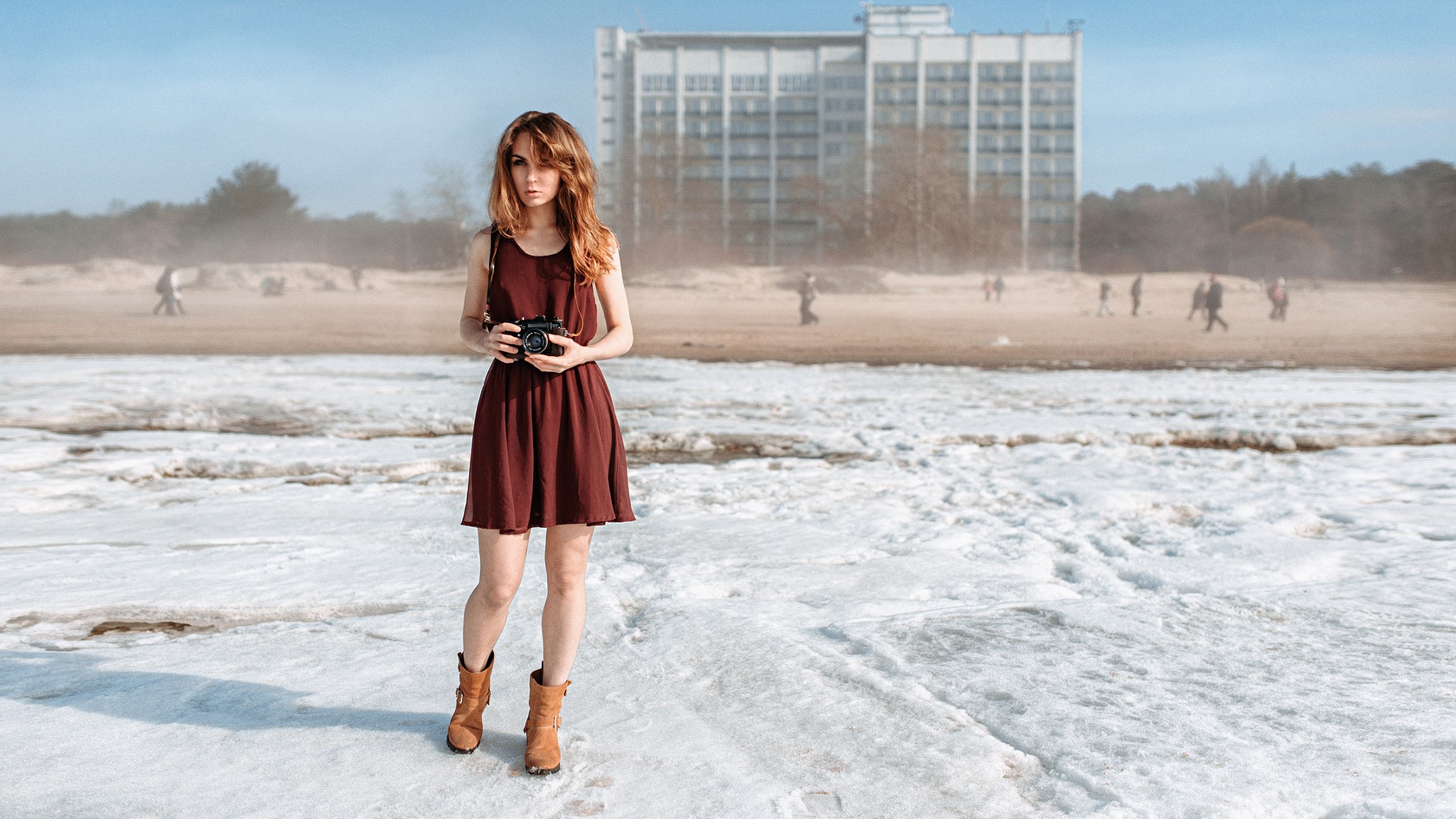 Woman with camera on a snowy beach with building HD Wallpaper