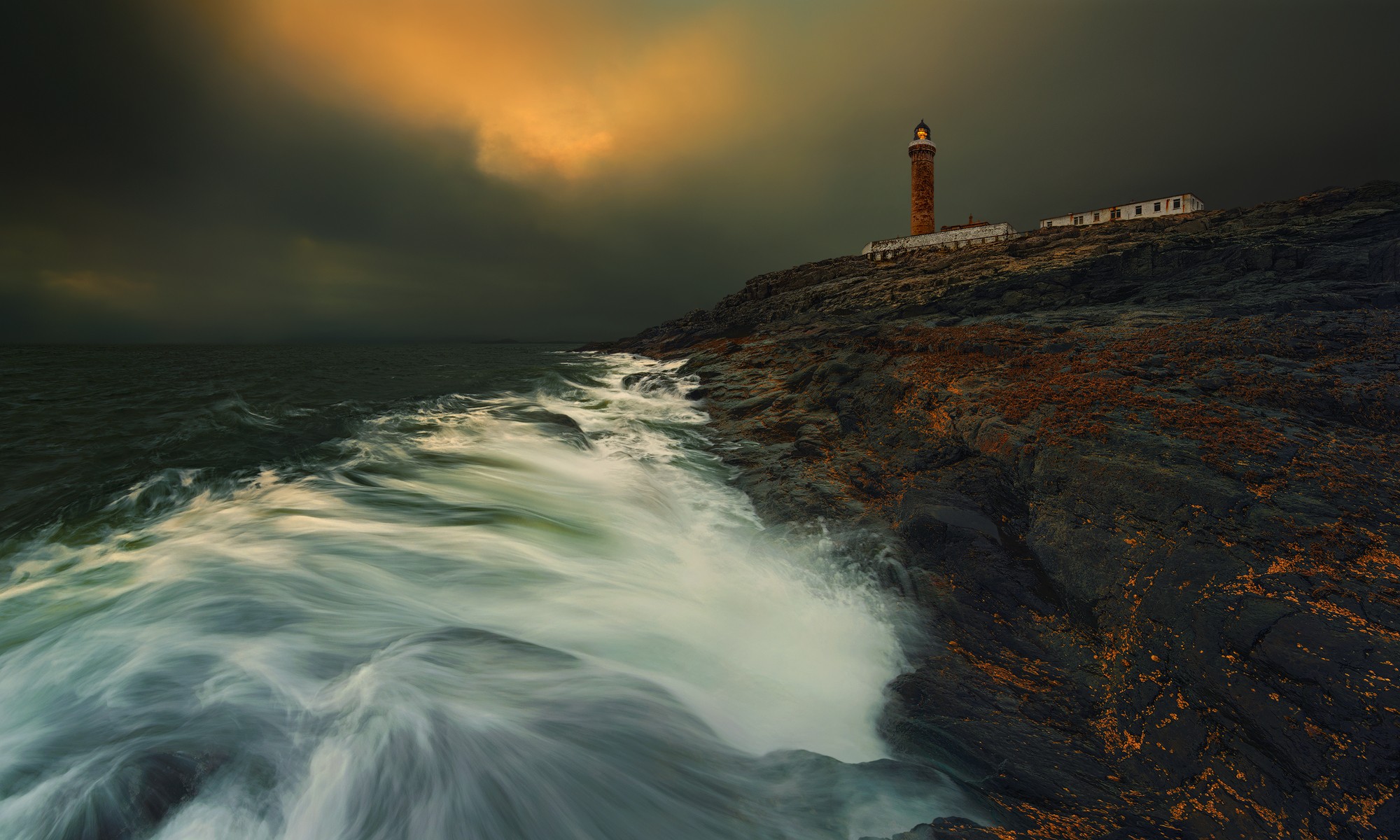 Lighthouse on a rocky coast with stormy seas HD Wallpaper
