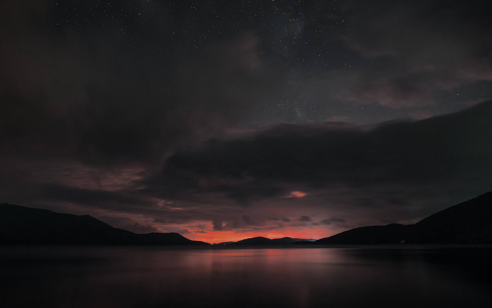 Dark lake and mountains under a starry, cloudy sky HD Wallpaper