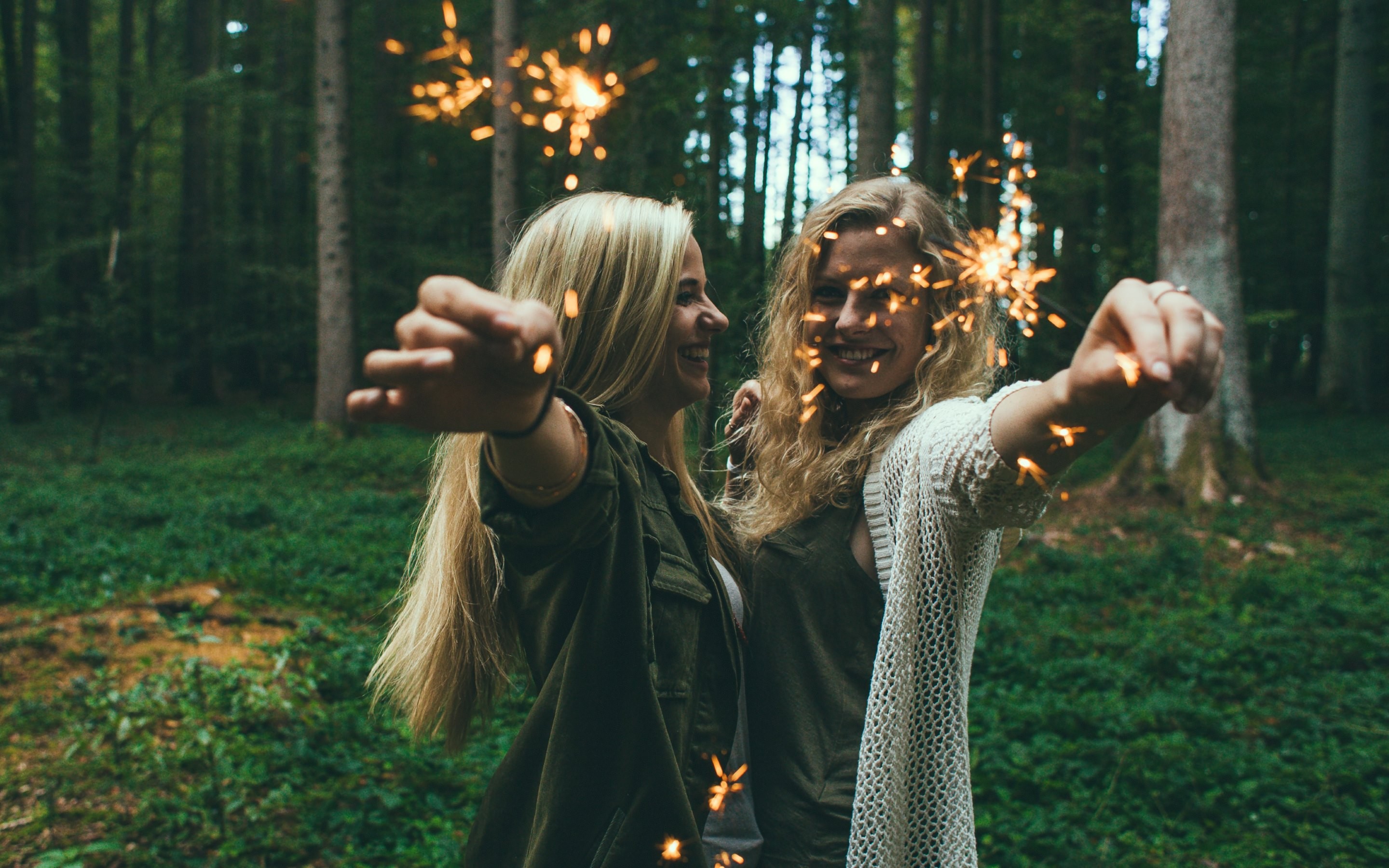 Two women holding sparklers in a forest HD Wallpaper