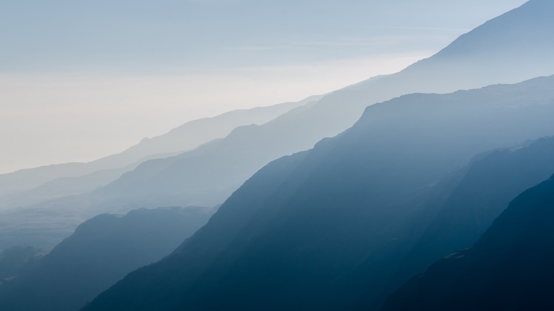 Layered mountains shrouded in mist under a pale sky HD Wallpaper