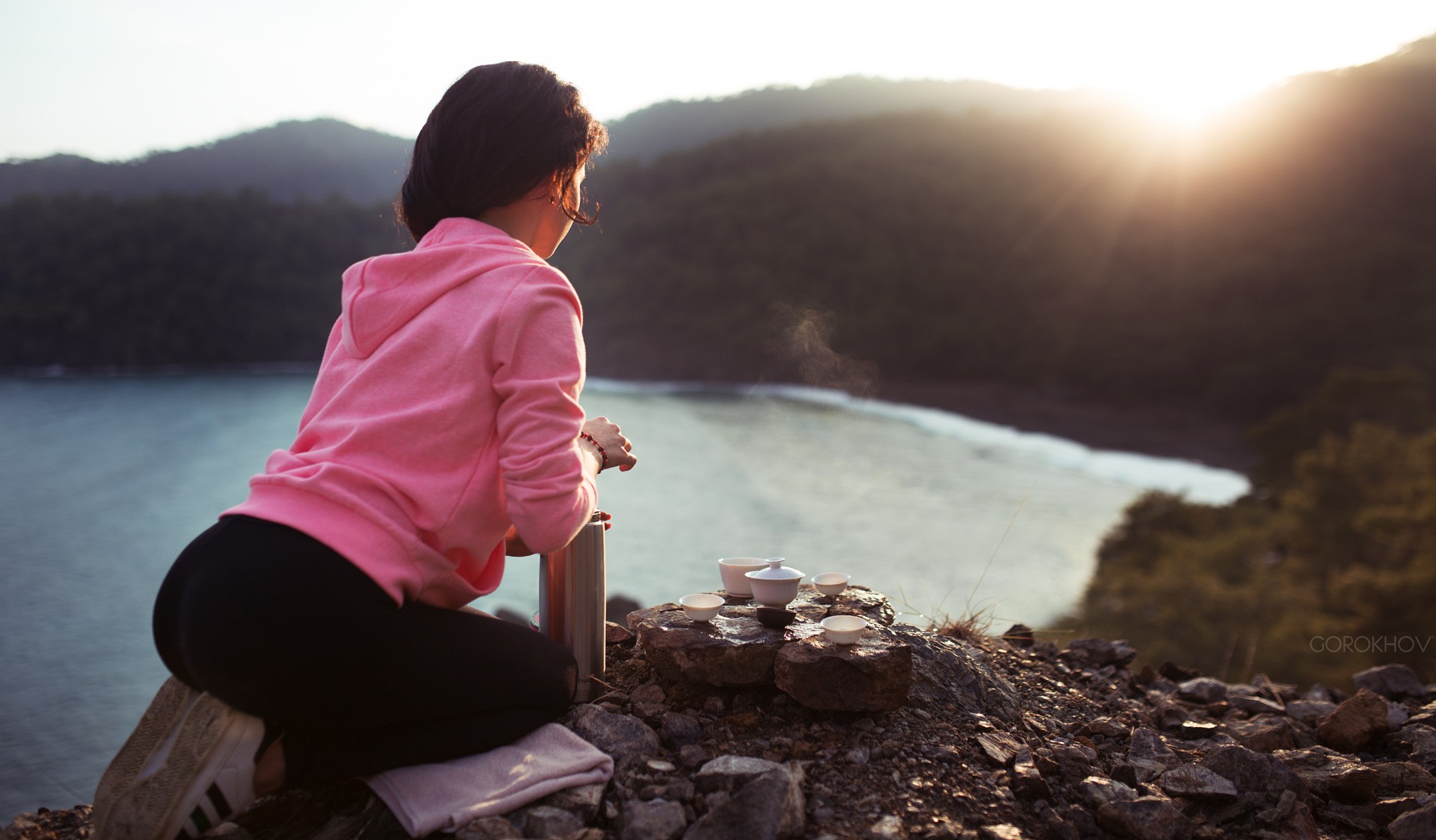 Woman in pink hoodie having tea by the lake at sunset HD Wallpaper