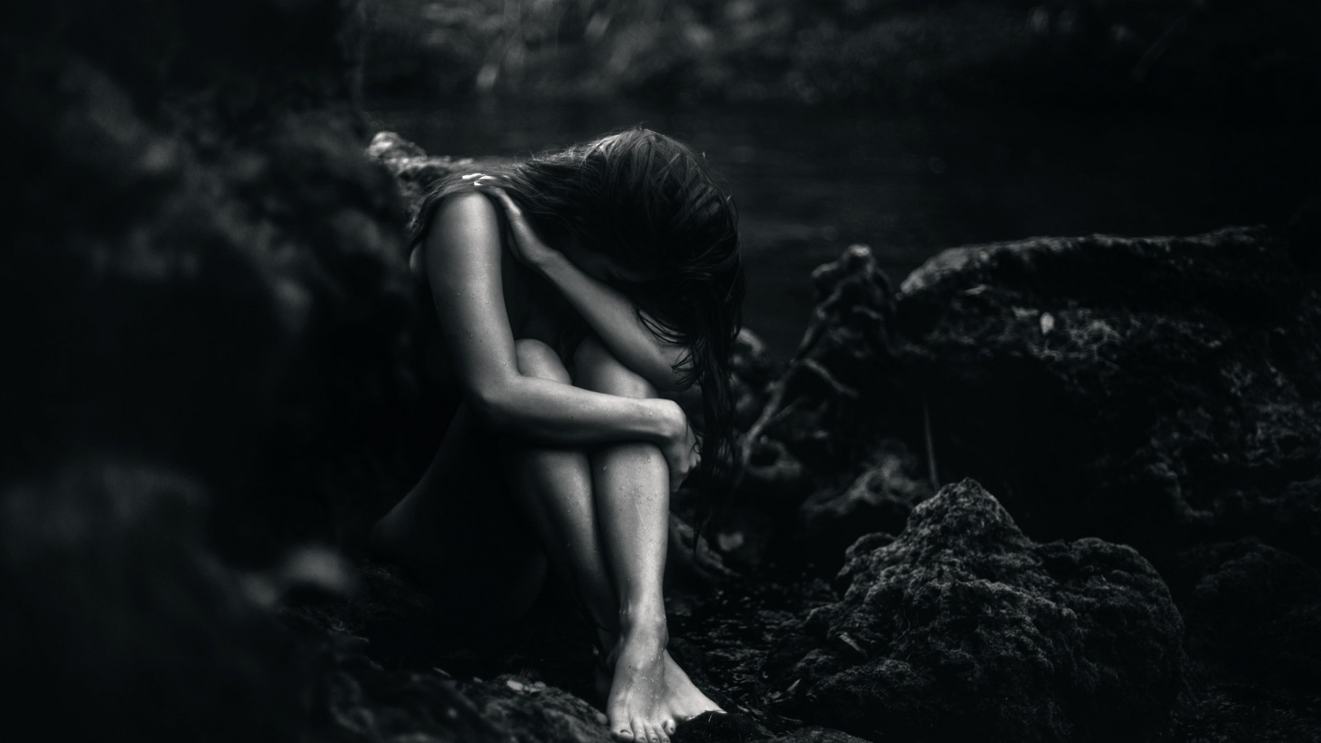 A woman sits alone in a dark, rocky environment HD Wallpaper