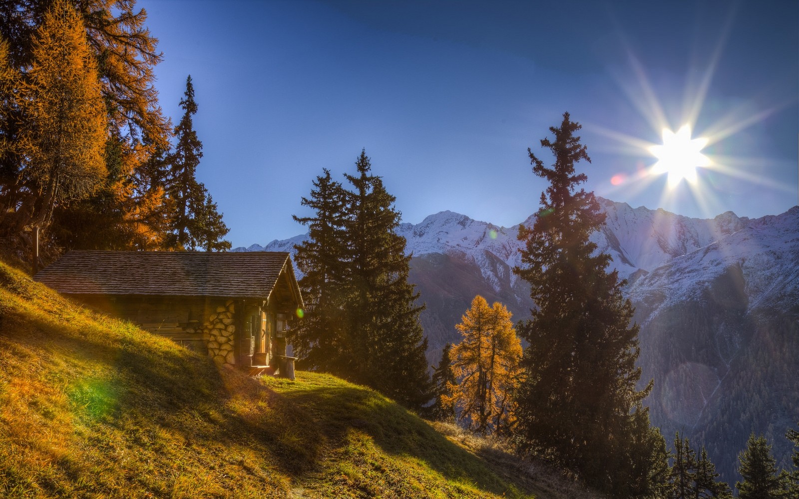 Wooden cabin on a grassy slope with snowy mountains HD Wallpaper
