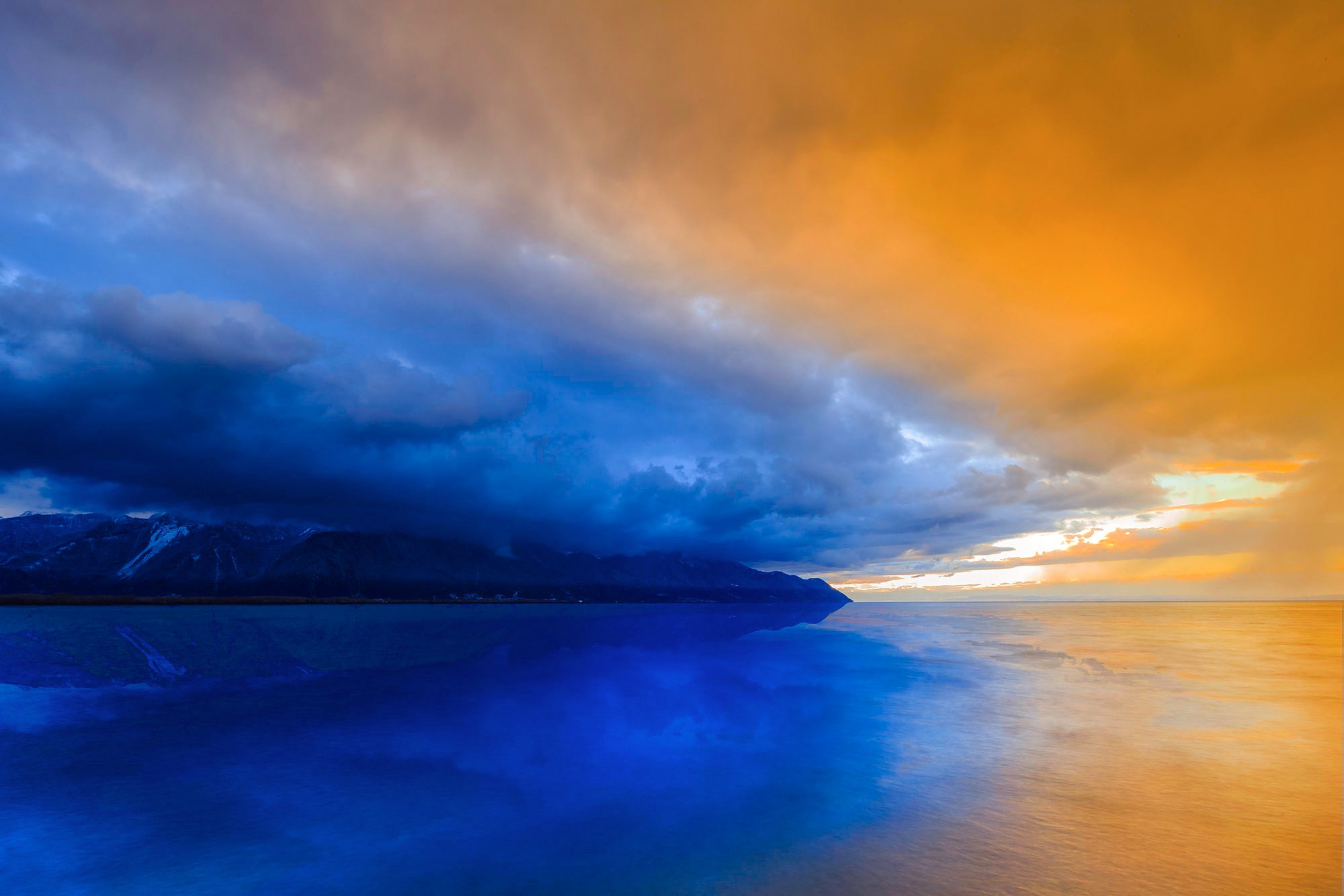 Sunset over a calm lake with mountains and clouds HD Wallpaper