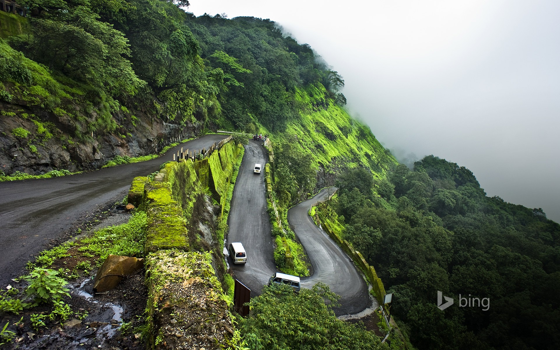 Winding mountain road with vehicles and fog HD Wallpaper