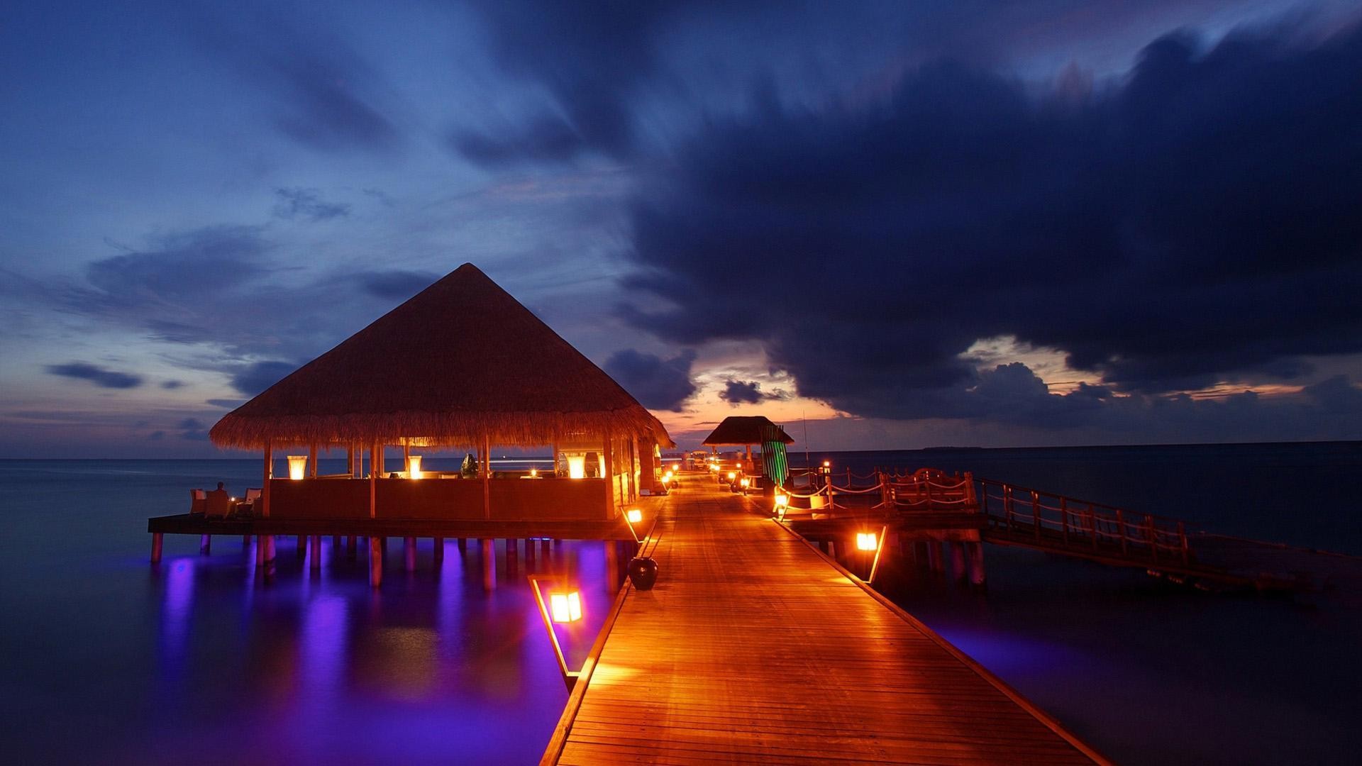 Overwater restaurant with thatched roof at dusk HD Wallpaper