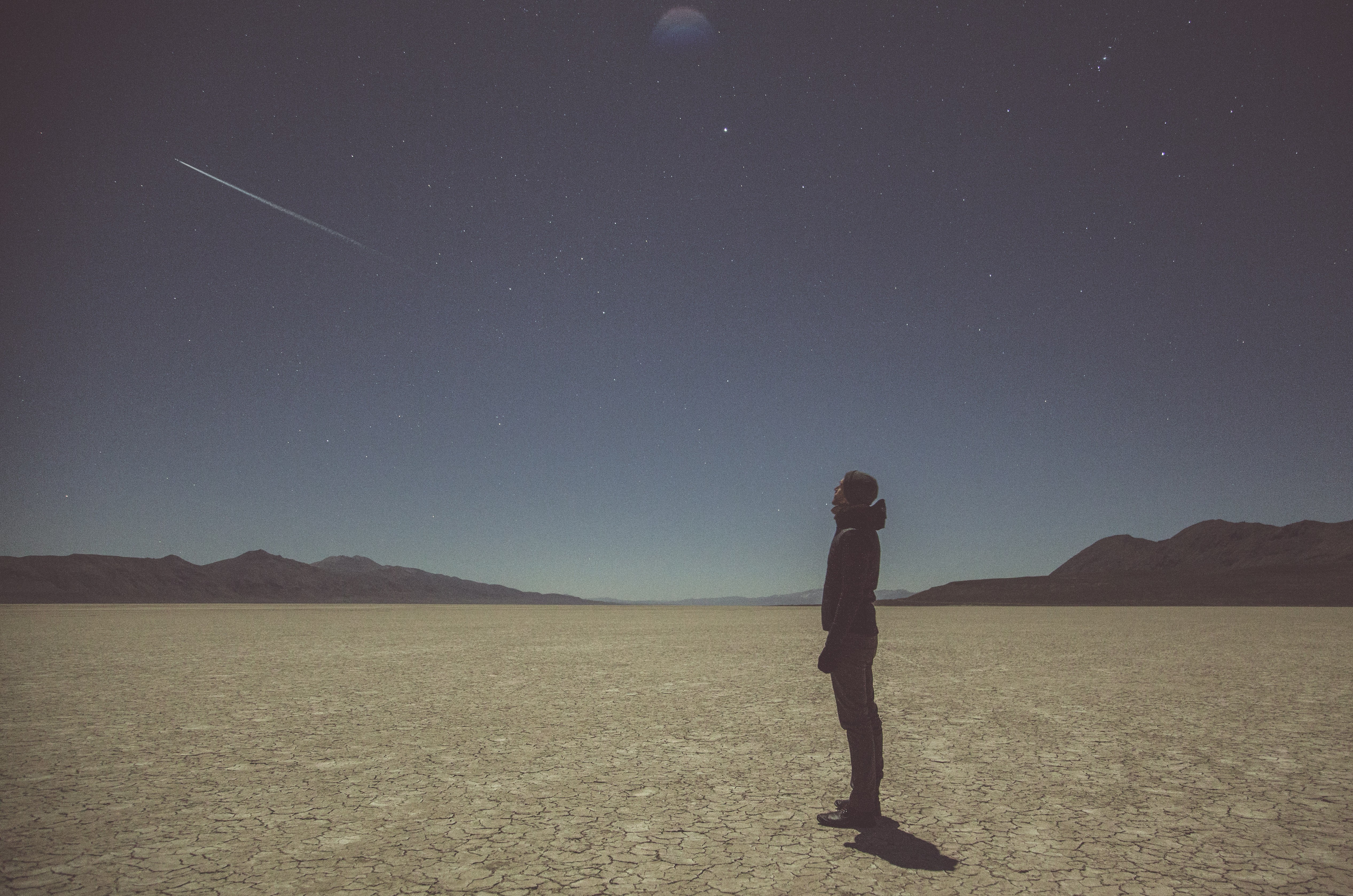 Man looking at a meteor shower in a desert HD Wallpaper