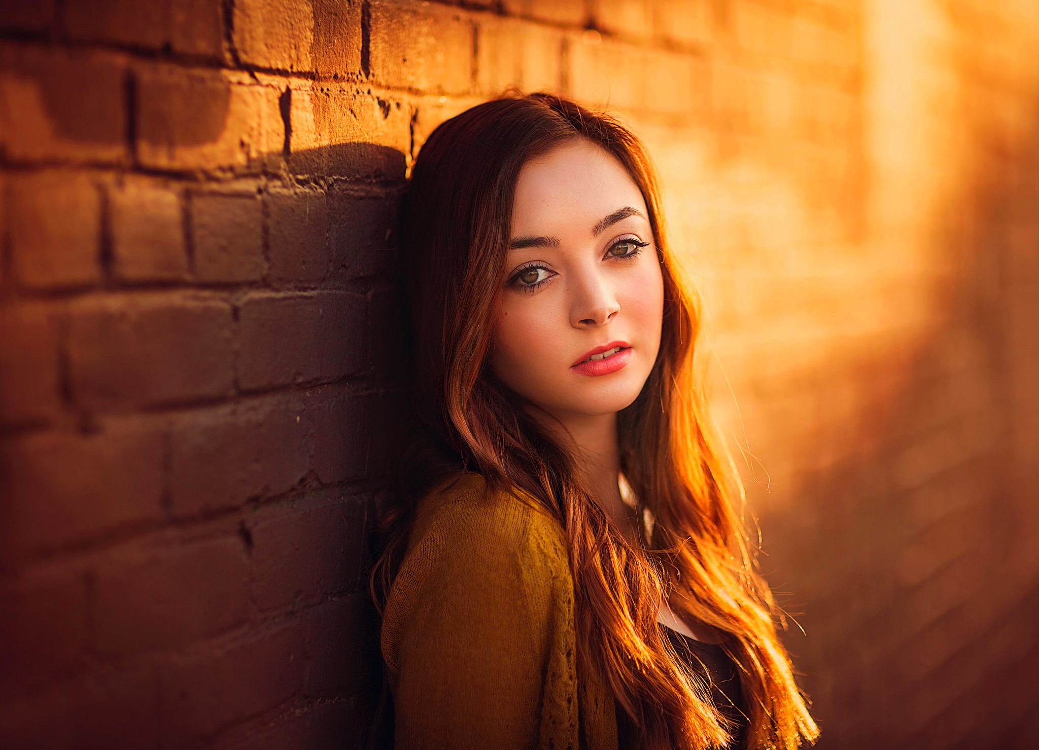 Portrait of a young woman leaning against a brick wall HD Wallpaper