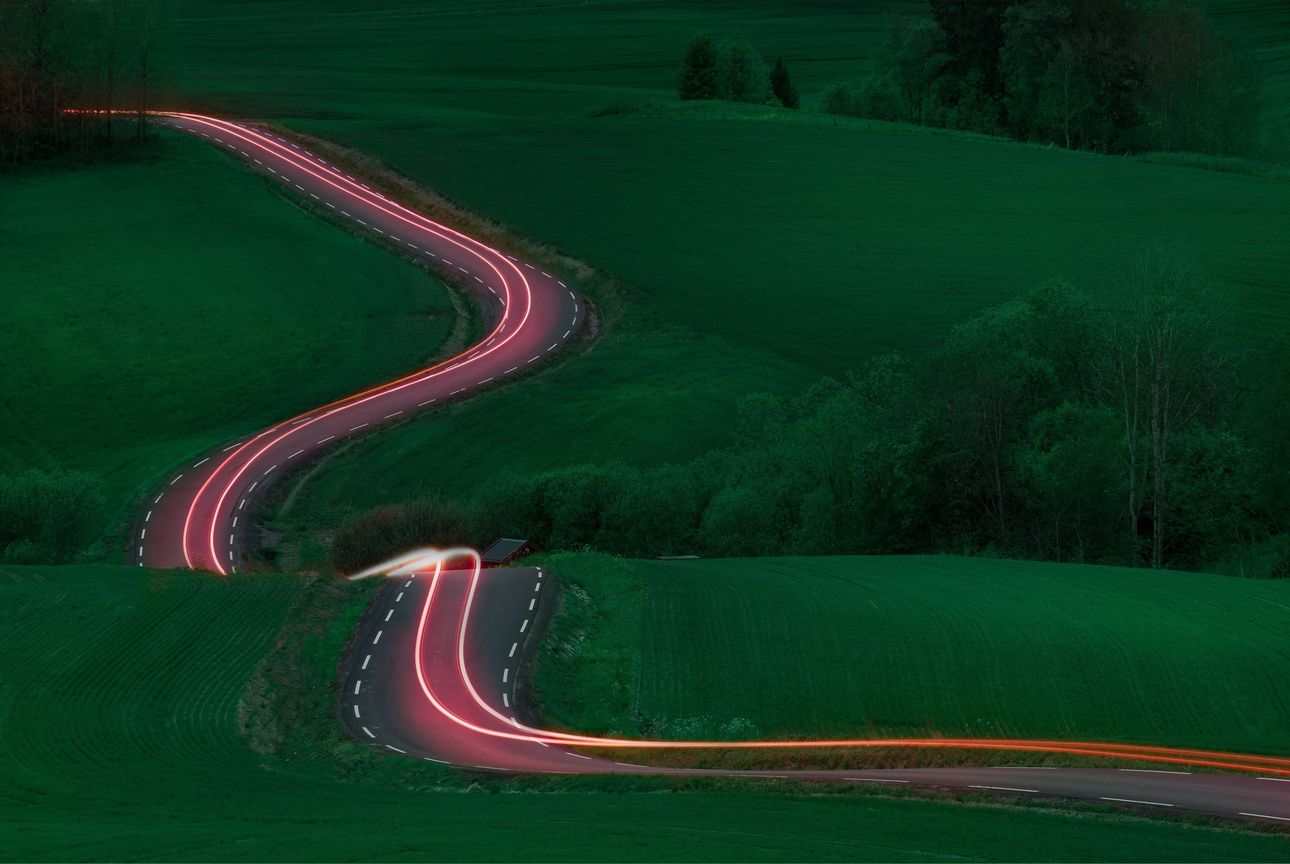 Long exposure of a winding road with light trails in a green landscape HD Wallpaper