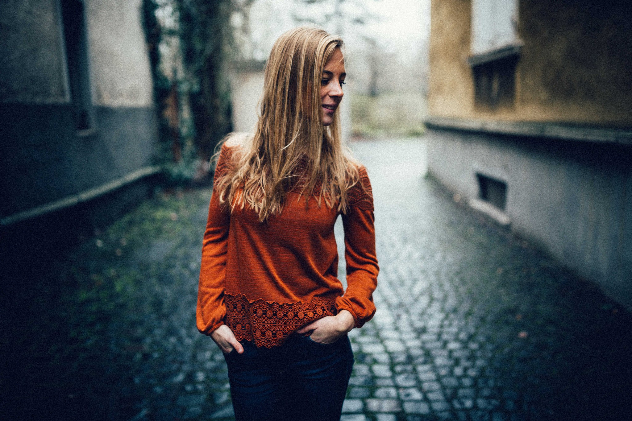 Woman with hands in pockets on a cobblestone street HD Wallpaper