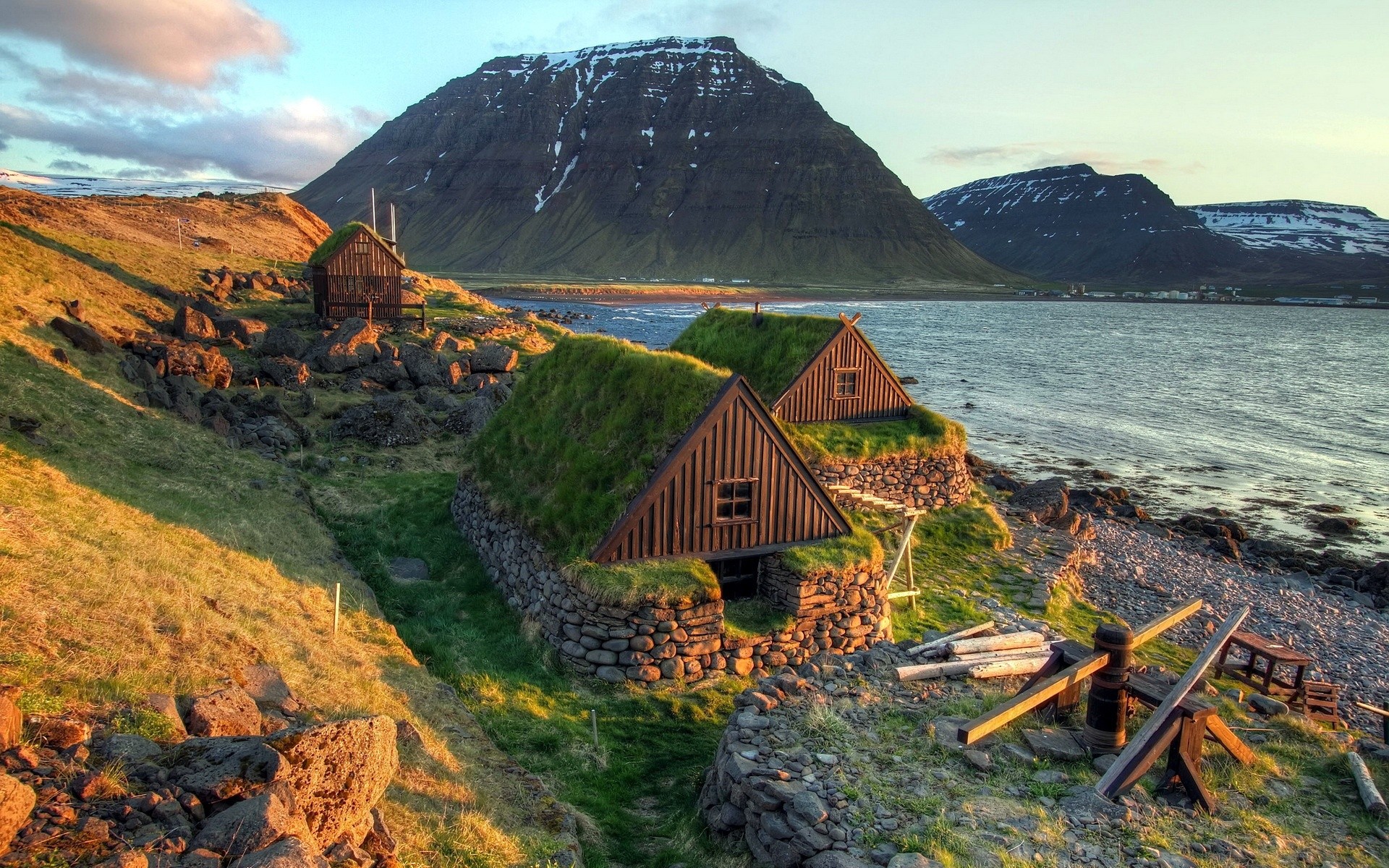 Icelandic turf houses on a rocky coast with mountains HD Wallpaper