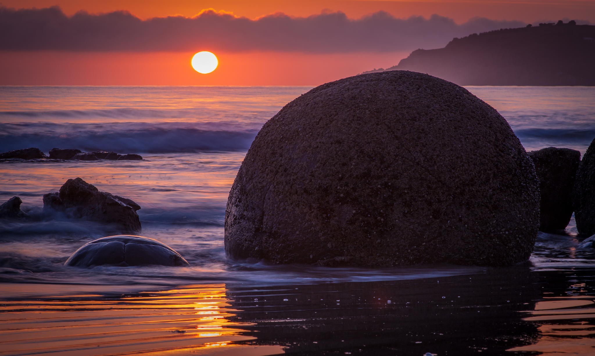 Sunset over the sea with large boulders on the beach HD Wallpaper
