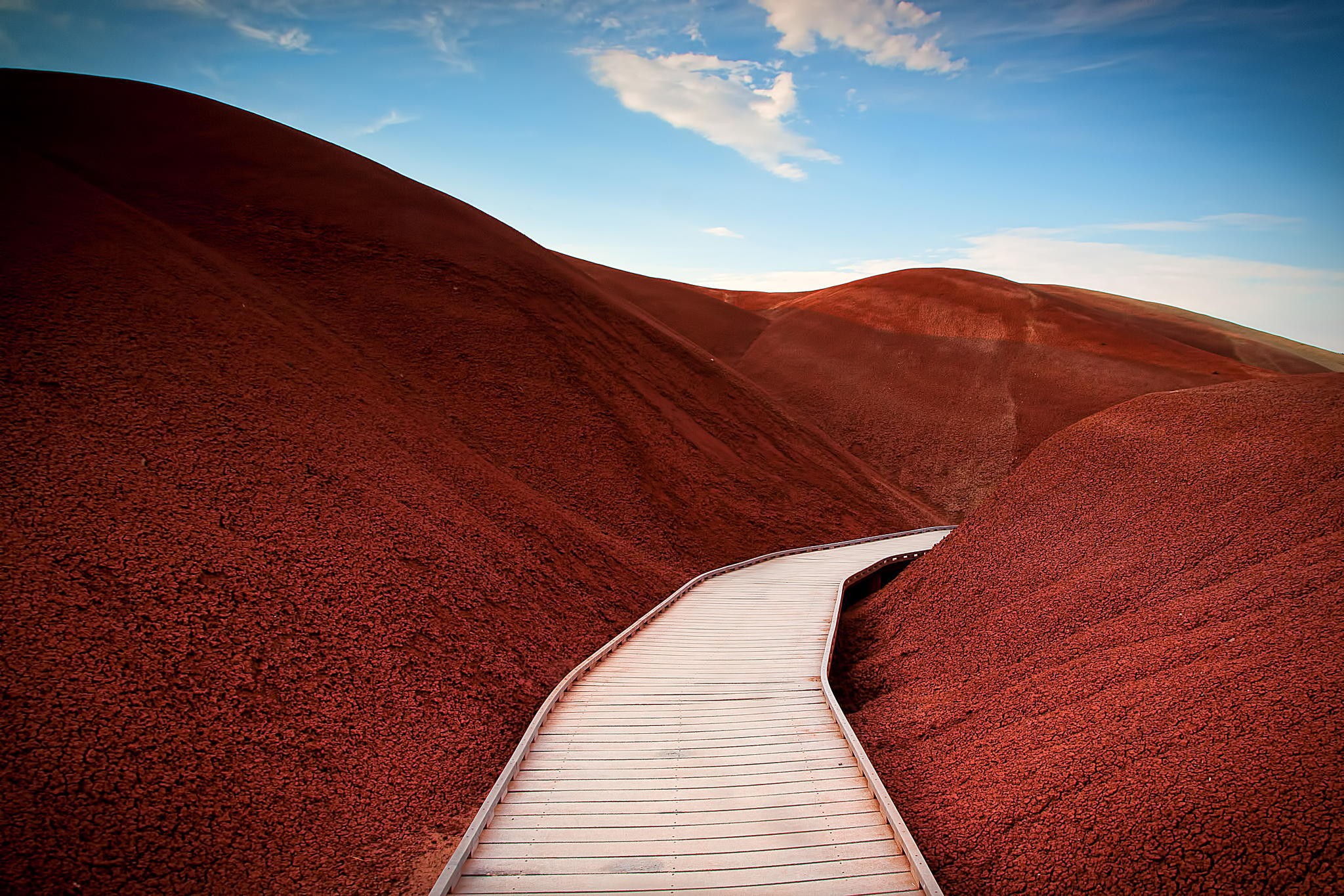 Wooden boardwalk through red desert hills HD Wallpaper