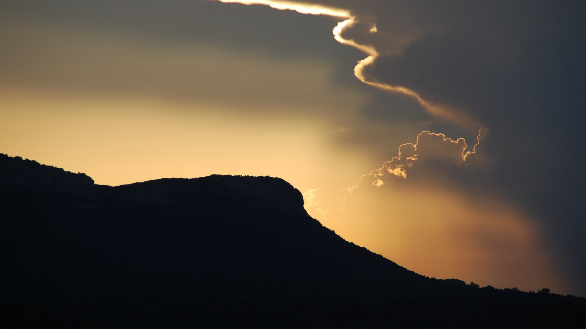 Silhouette of hills against a dramatic sunset sky with clouds HD Wallpaper