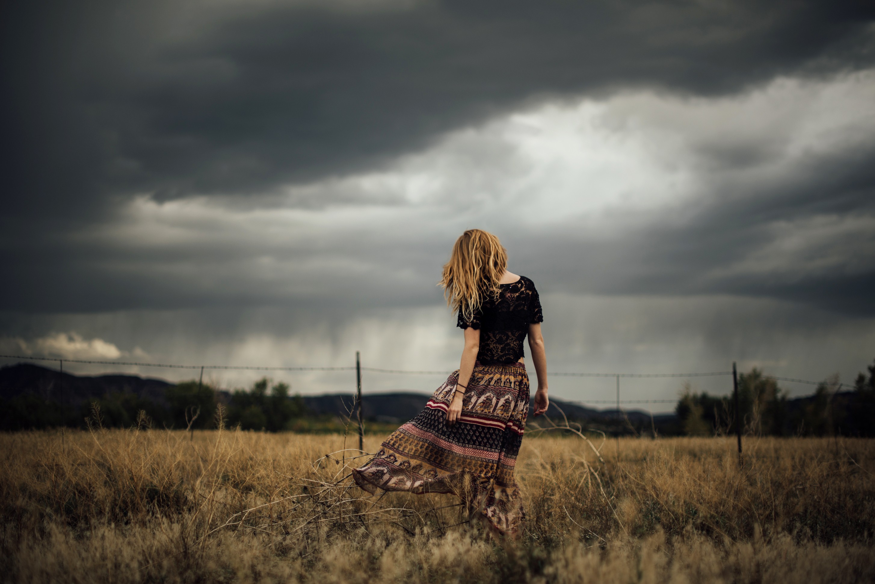 Woman in a field under stormy clouds HD Wallpaper