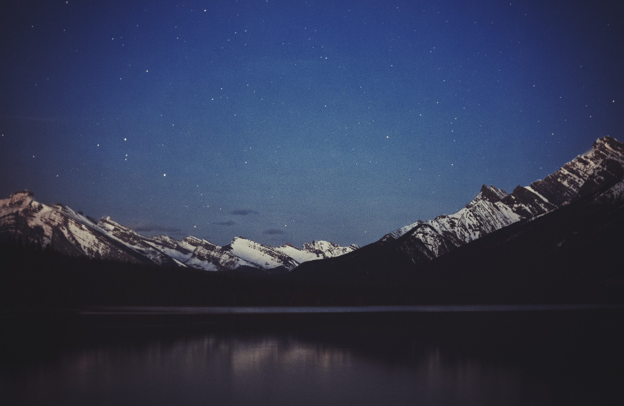 Snow-capped mountains reflected in a lake under a starry night sky HD Wallpaper