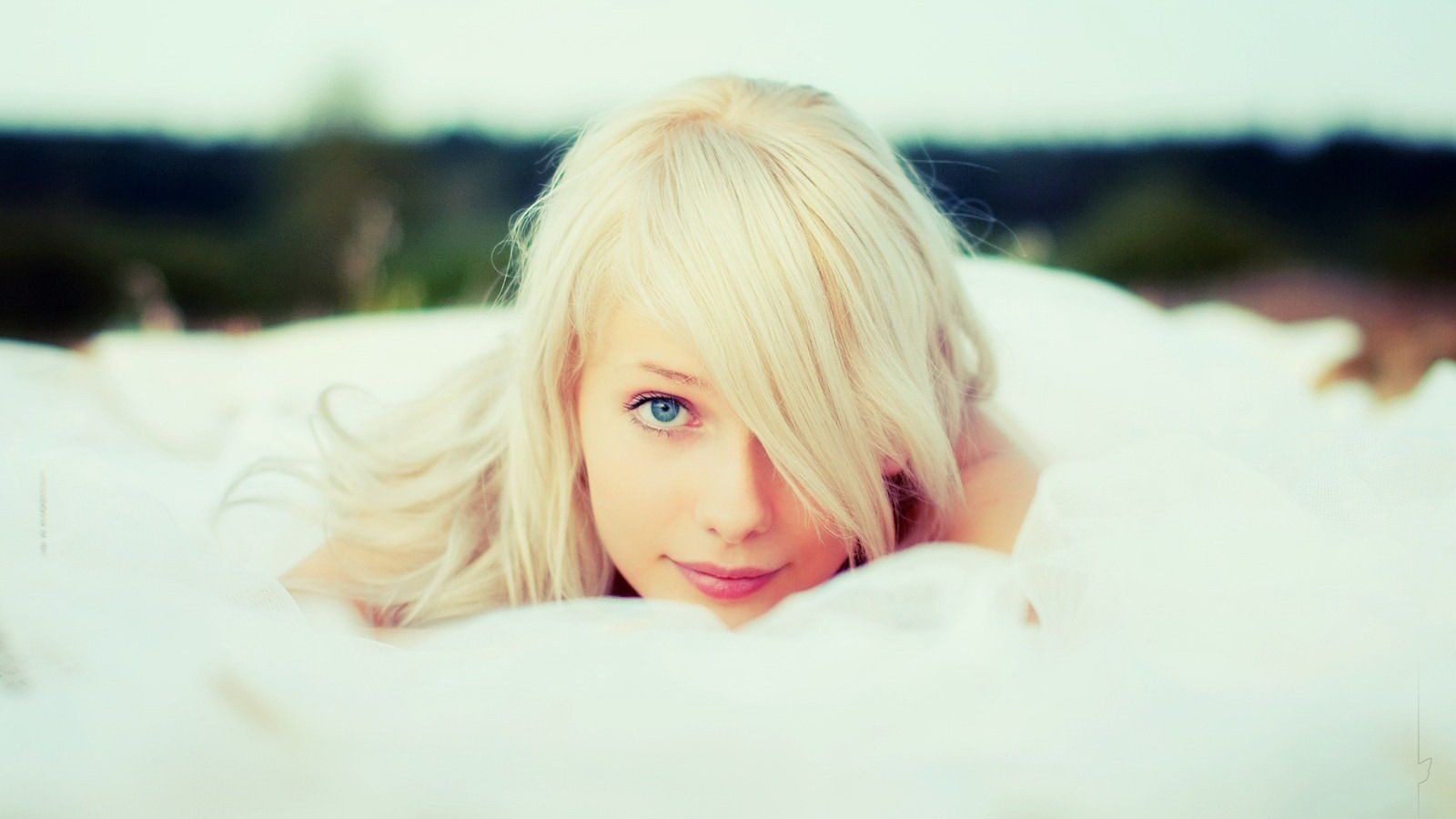 Blonde woman lying on white fabric looking at viewer HD Wallpaper