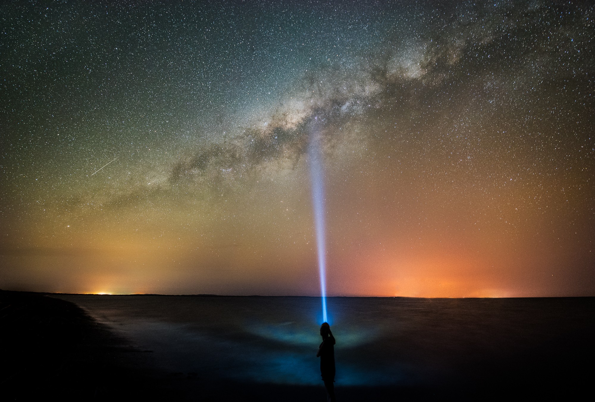 Person shining flashlight at the Milky Way over the ocean HD Wallpaper