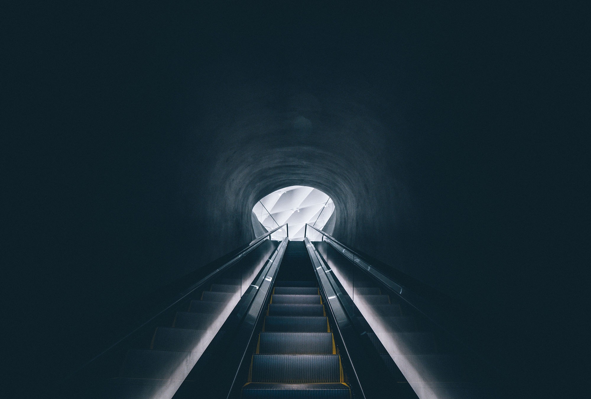Escalator leading to a bright opening in a dark tunnel HD Wallpaper