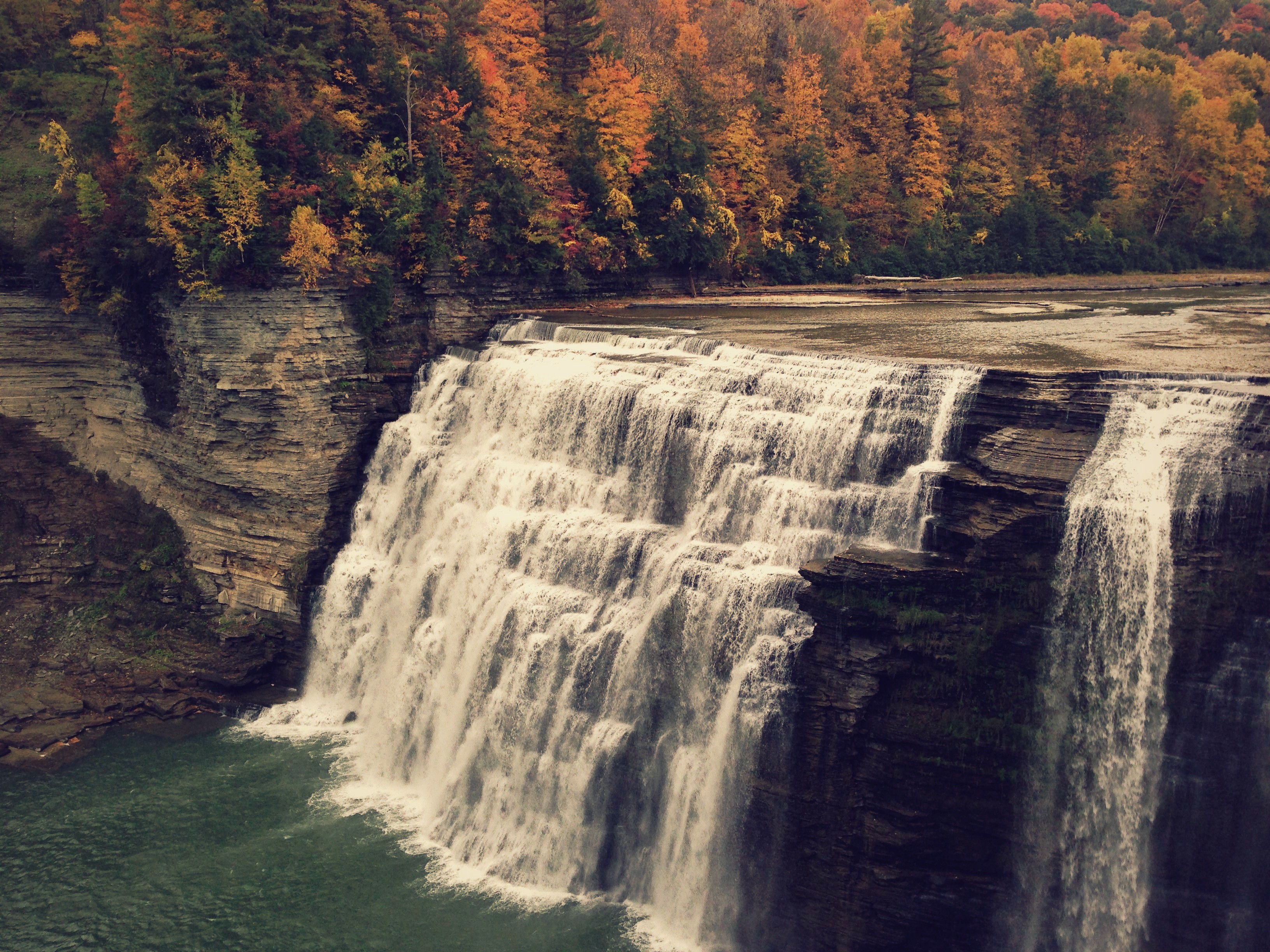 Waterfall cascading over layered rocks with autumn forest HD Wallpaper
