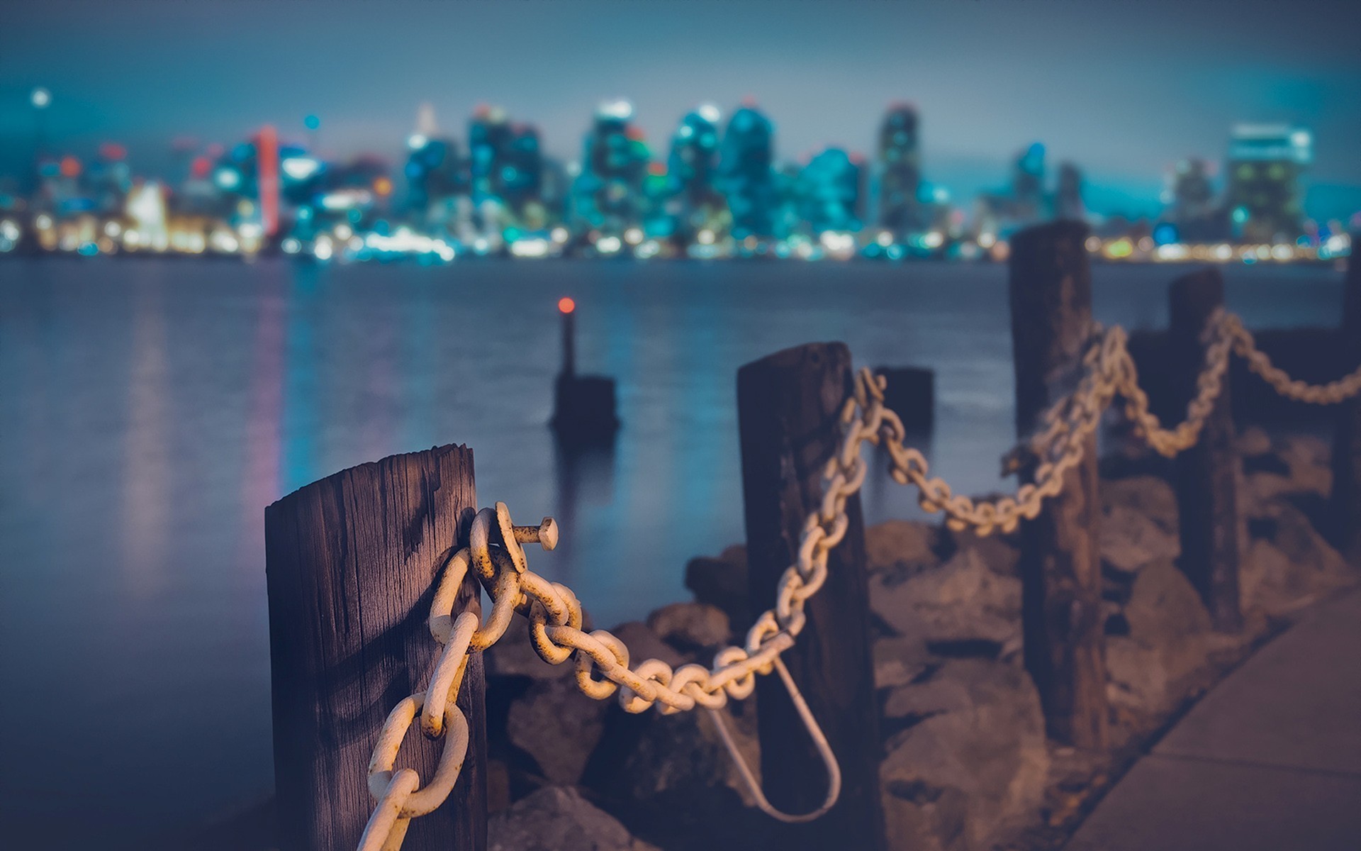 City skyline across water at night with chain fence HD Wallpaper