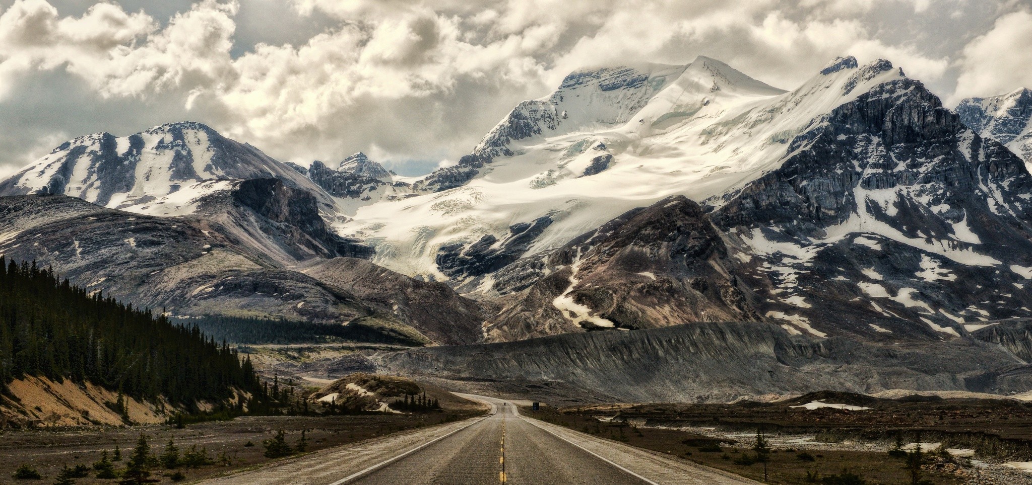 Road leading to snow-capped mountains under cloudy sky HD Wallpaper